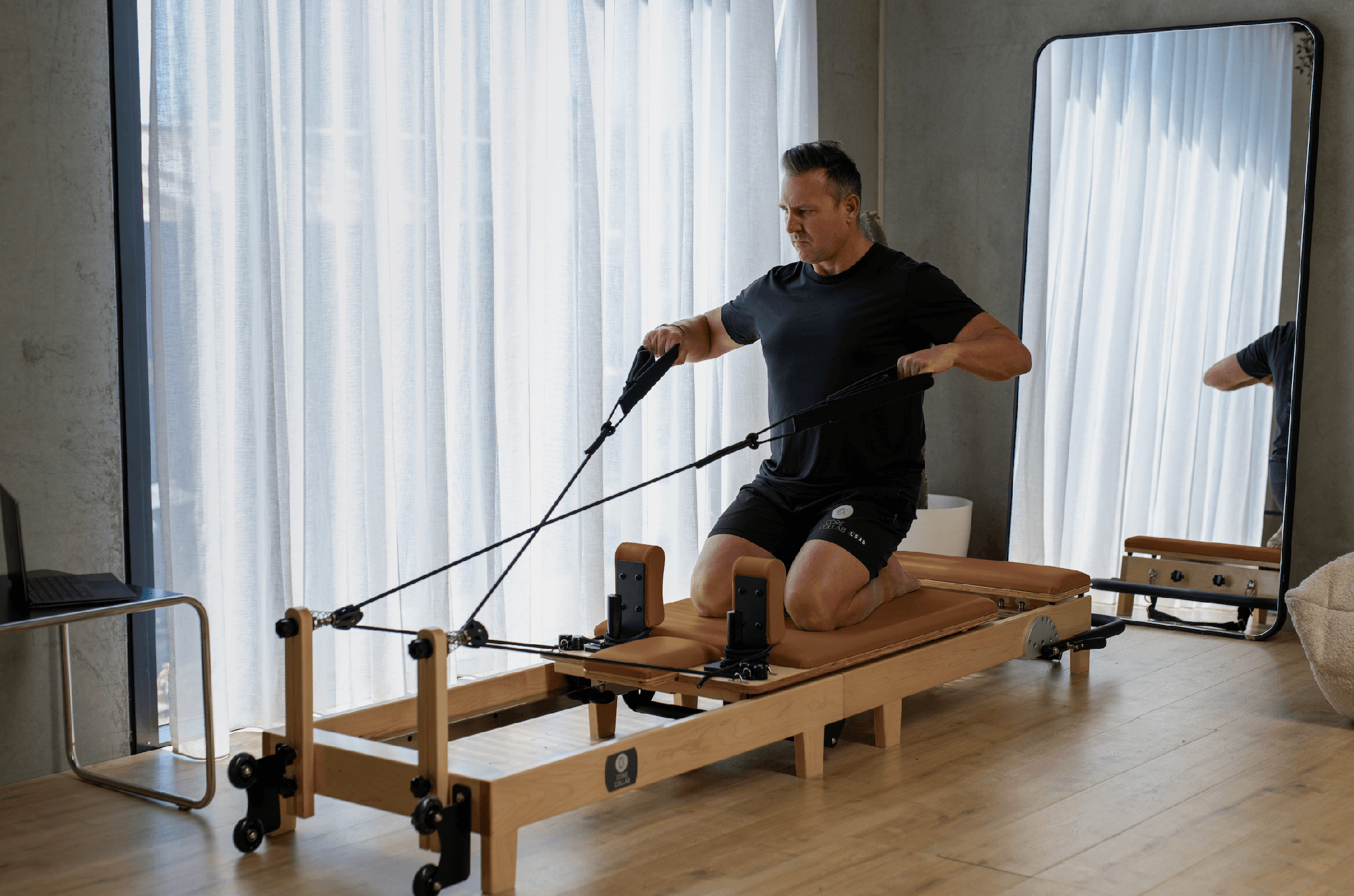 Eco Folding Pilates Reformer with a natural maple wood frame, tan padded carriage and black straps in use