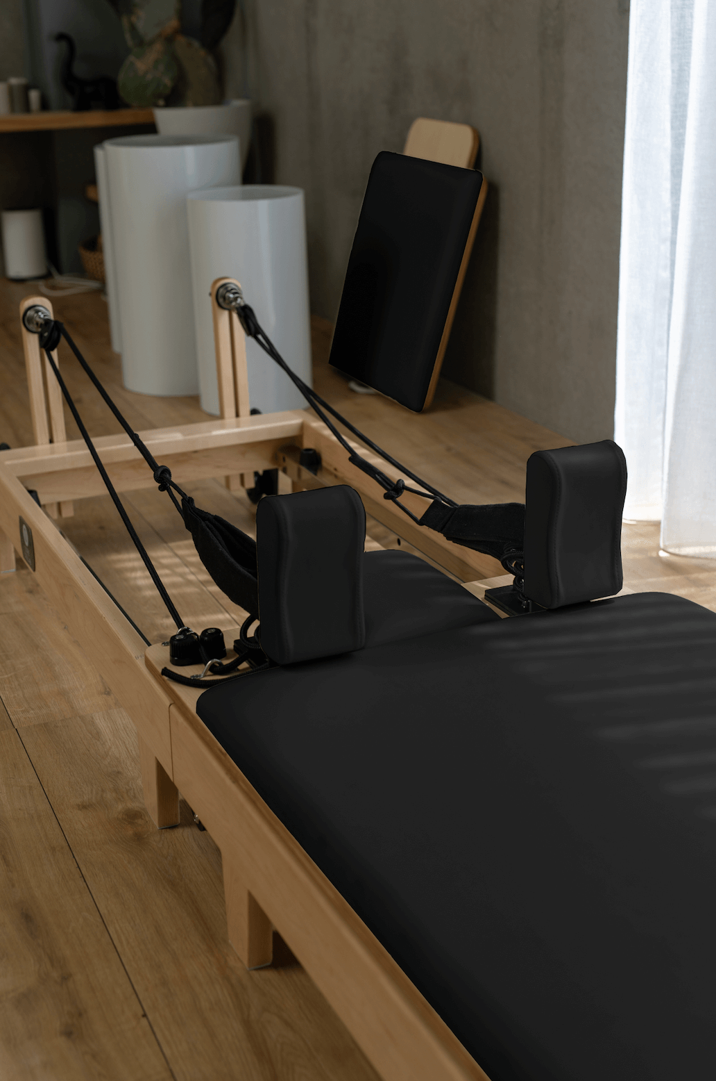 Eco Folding Pilates Reformer with a natural maple wood frame, black padded carriage, adjustable footbar, straps and springs.