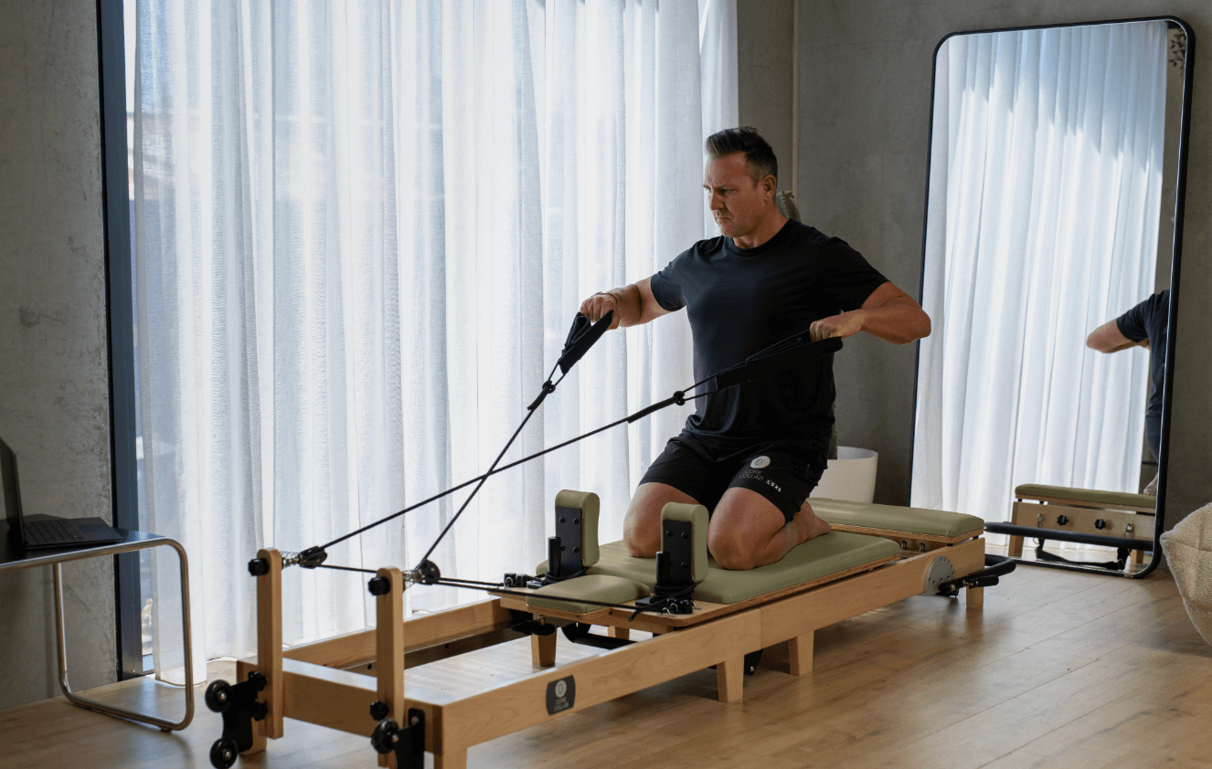 Eco Folding Pilates Reformer with a natural maple wood frame, olive-green padded carriage, black straps and adjustable risers.