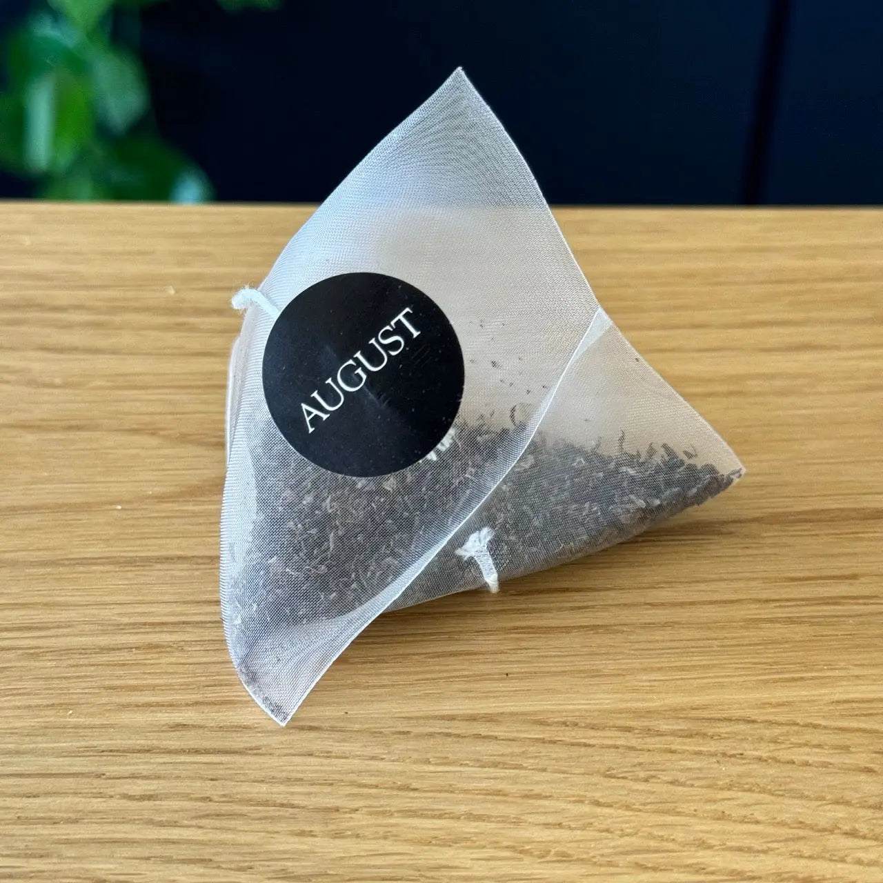 Essentials Black Tea in a translucent pyramid tea bag with loose black tea leaves and August label
