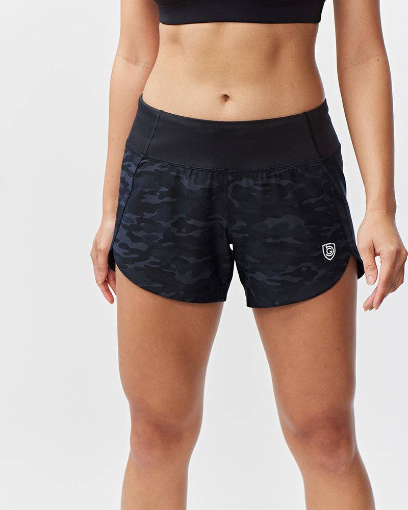 Excel Women's Workout Shorts in black stretch fabric with a subtle dark camouflage pattern, wide waistband and logo detail