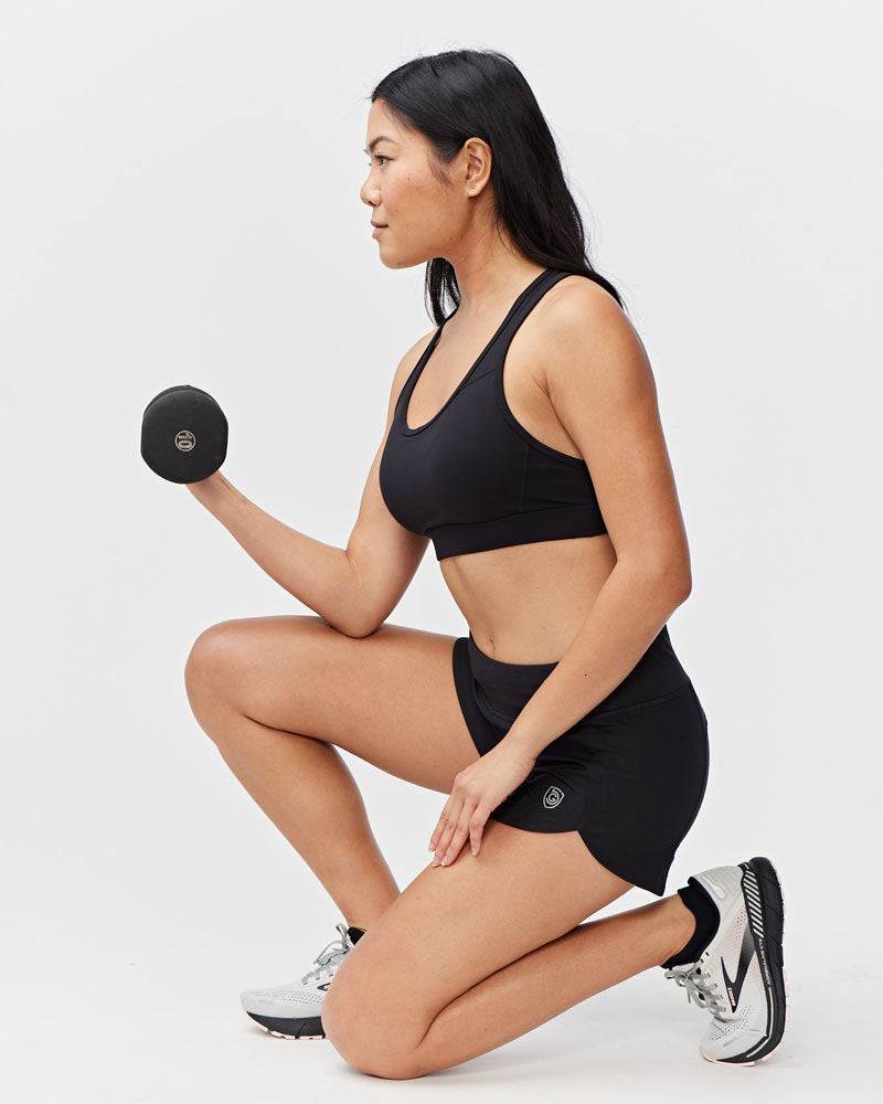 Excel Women's Workout Shorts in black stretch fabric, worn with a matching sports bra and featuring a small side logo