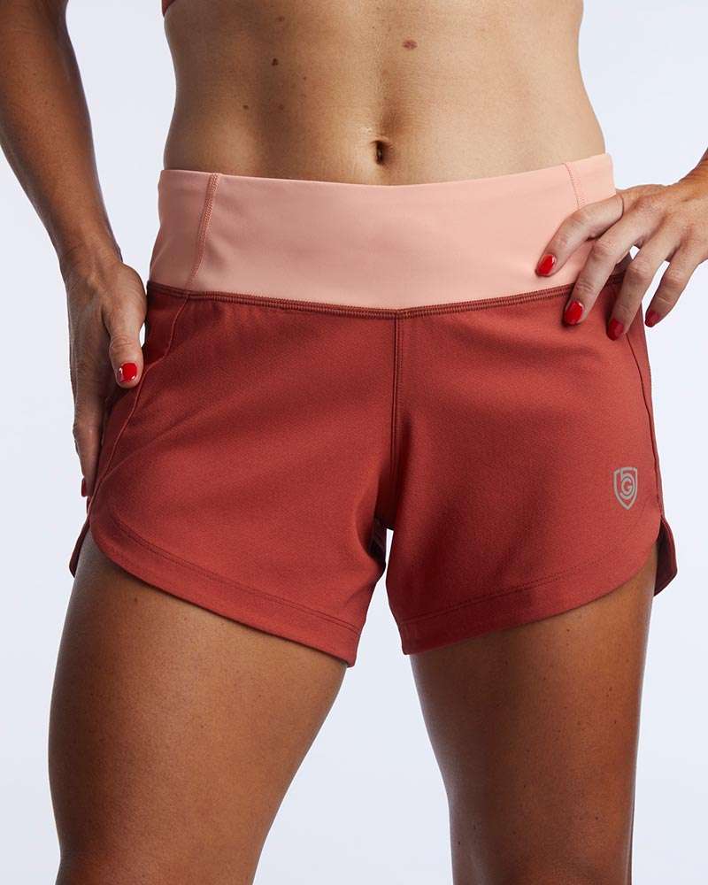 Excel Women's Workout Shorts in rust red stretch fabric with a pale pink wide waistband and small logo