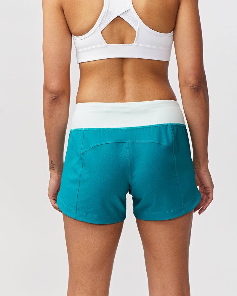Excel Women's Workout Shorts in solid teal stretch fabric with a wide white waistband and curved hem