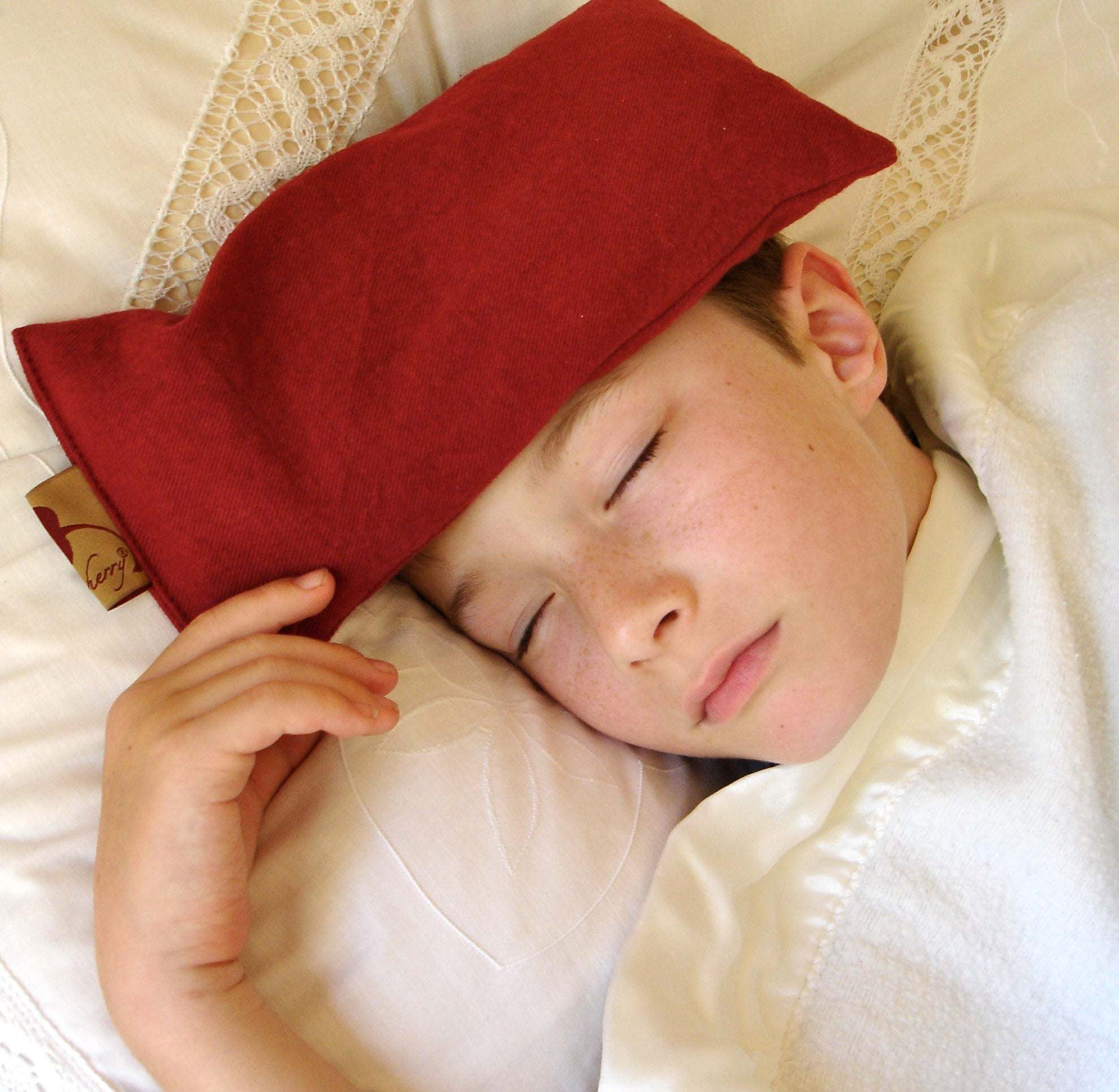 Eye Pillow in solid deep red plush fabric resting on a child's closed eyes, rectangular shape with soft texture.