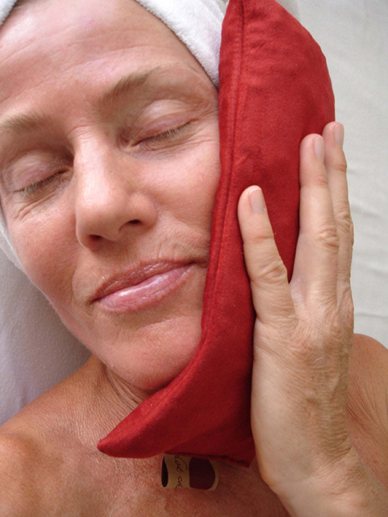 Eye Pillow in plush red ultra-suede being held gently against a person's face for comfort and relaxation.