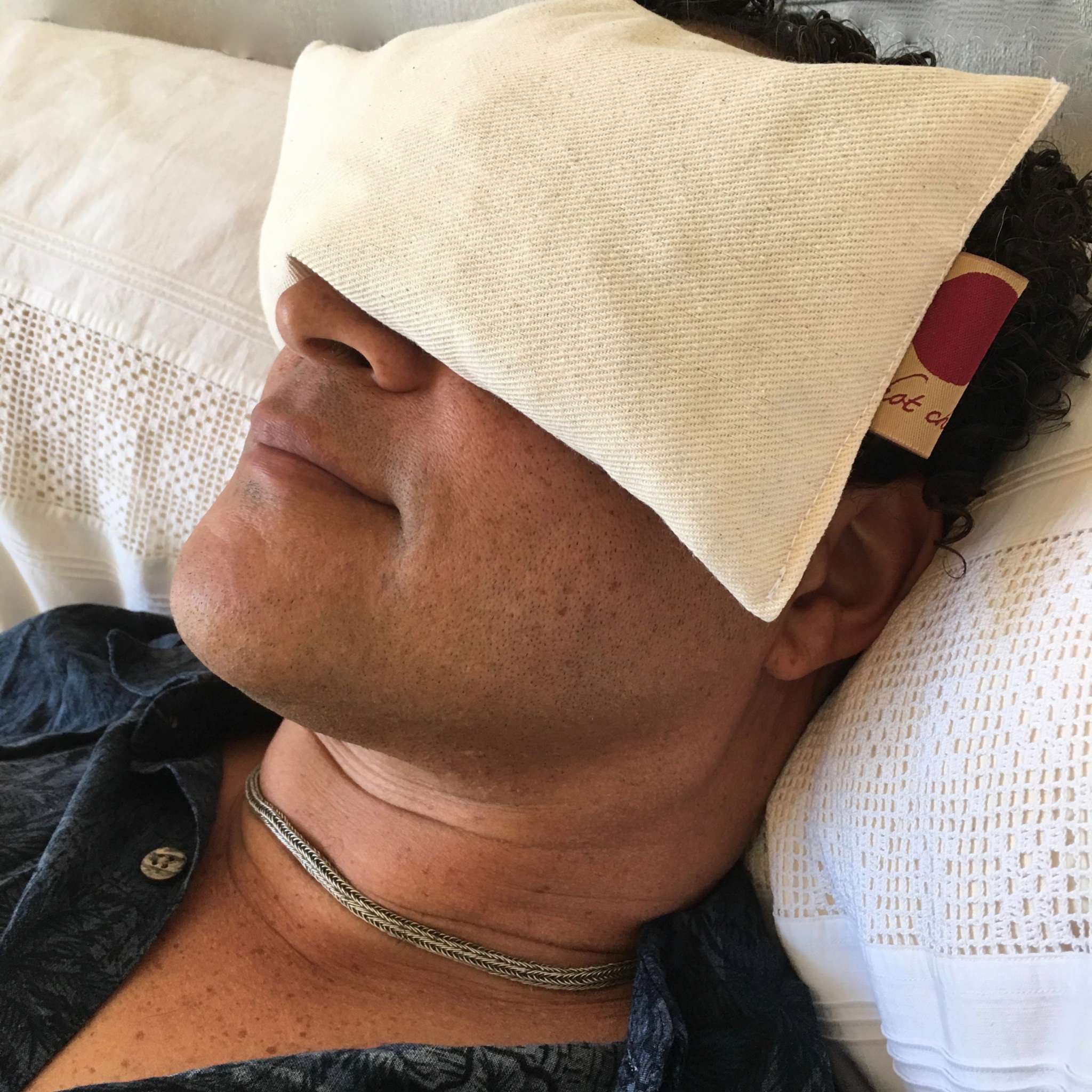 Eye Pillow in natural unbleached cream fabric, a soft rectangular cover resting over the eyes with a small side tag