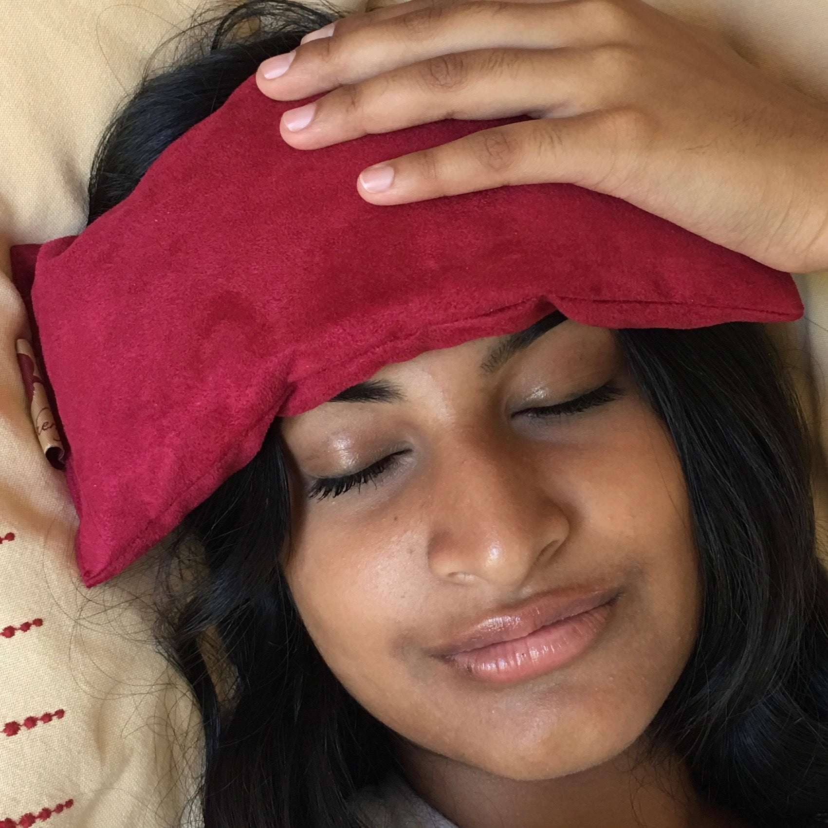 Eye Pillow in plush red ultra-suede fabric resting on a woman's forehead, highlighting comfort and relaxation.