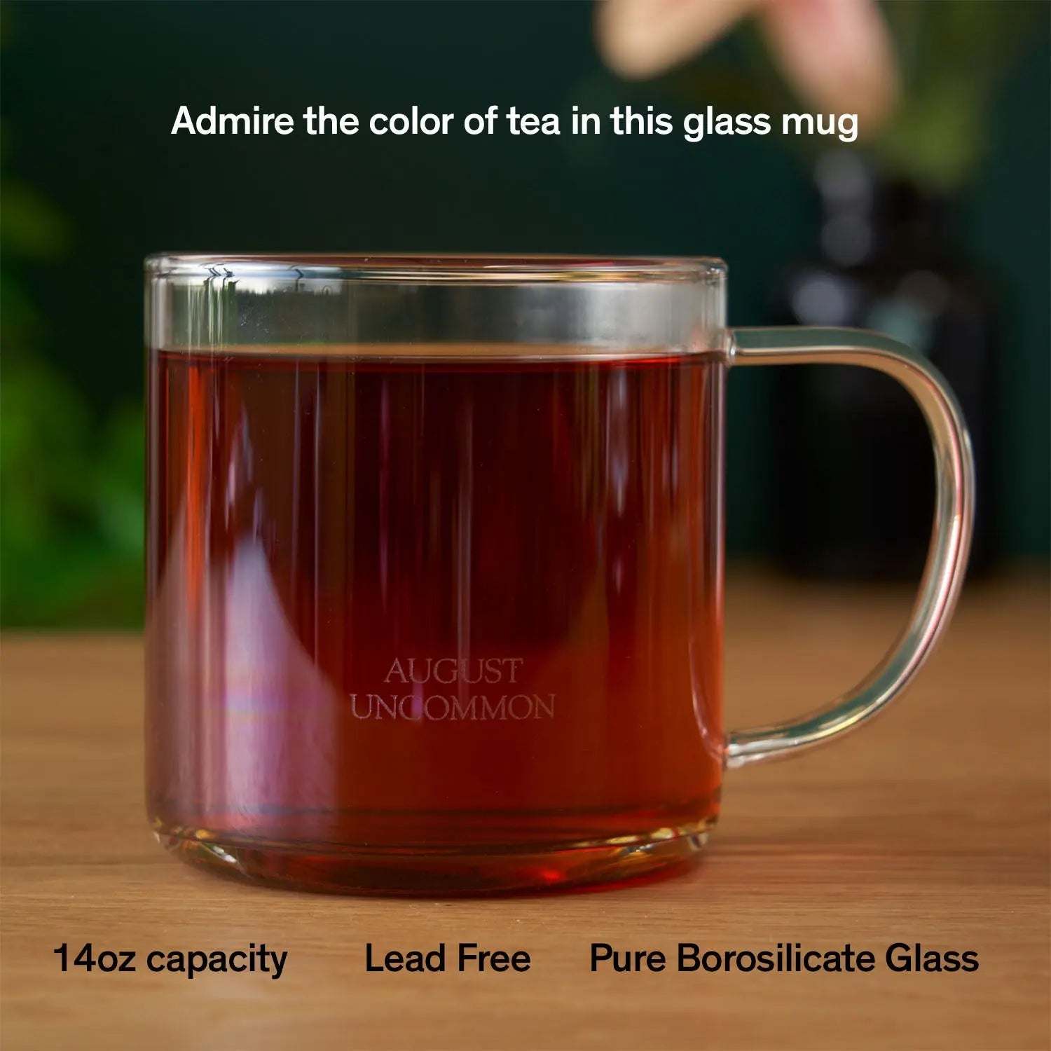 Glass Mug in clear borosilicate glass, filled with dark amber tea, with a rounded handle and etched logo