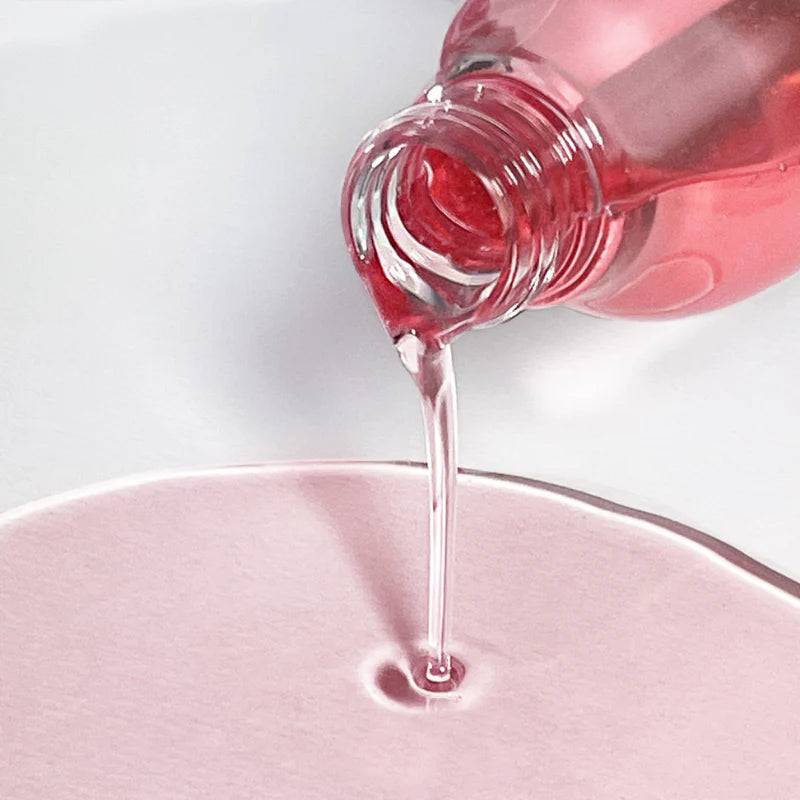 Glow Guava Facial Cleanser being poured from a translucent pink bottle showing the clear liquid and pink gel layers with smooth texture.