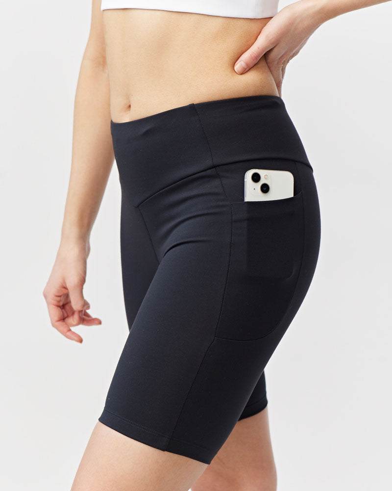 Go Again Bike Short in black stretch knit, fitted to mid-thigh with a high waistband and side pocket holding a phone