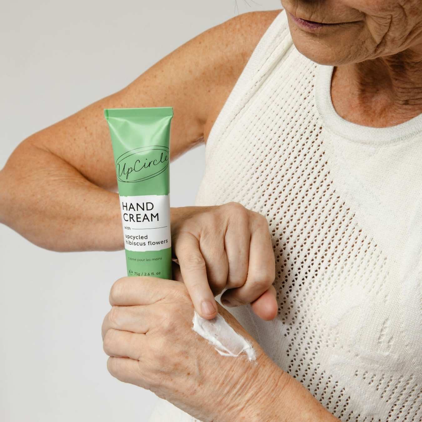 Hand Cream with Hibiscus Flowers in a green aluminum tube, applied as a white cream to mature hands