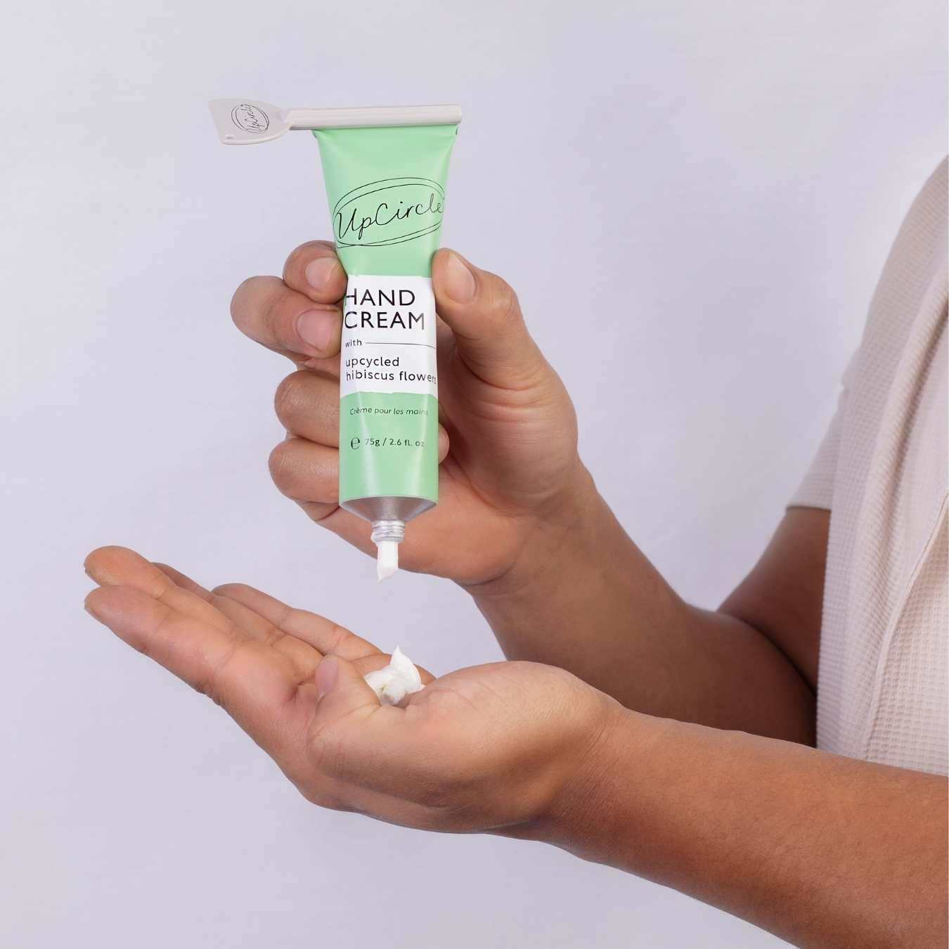 Hand Cream with Hibiscus Flowers in a mint green aluminum tube, dispensed onto an open hand