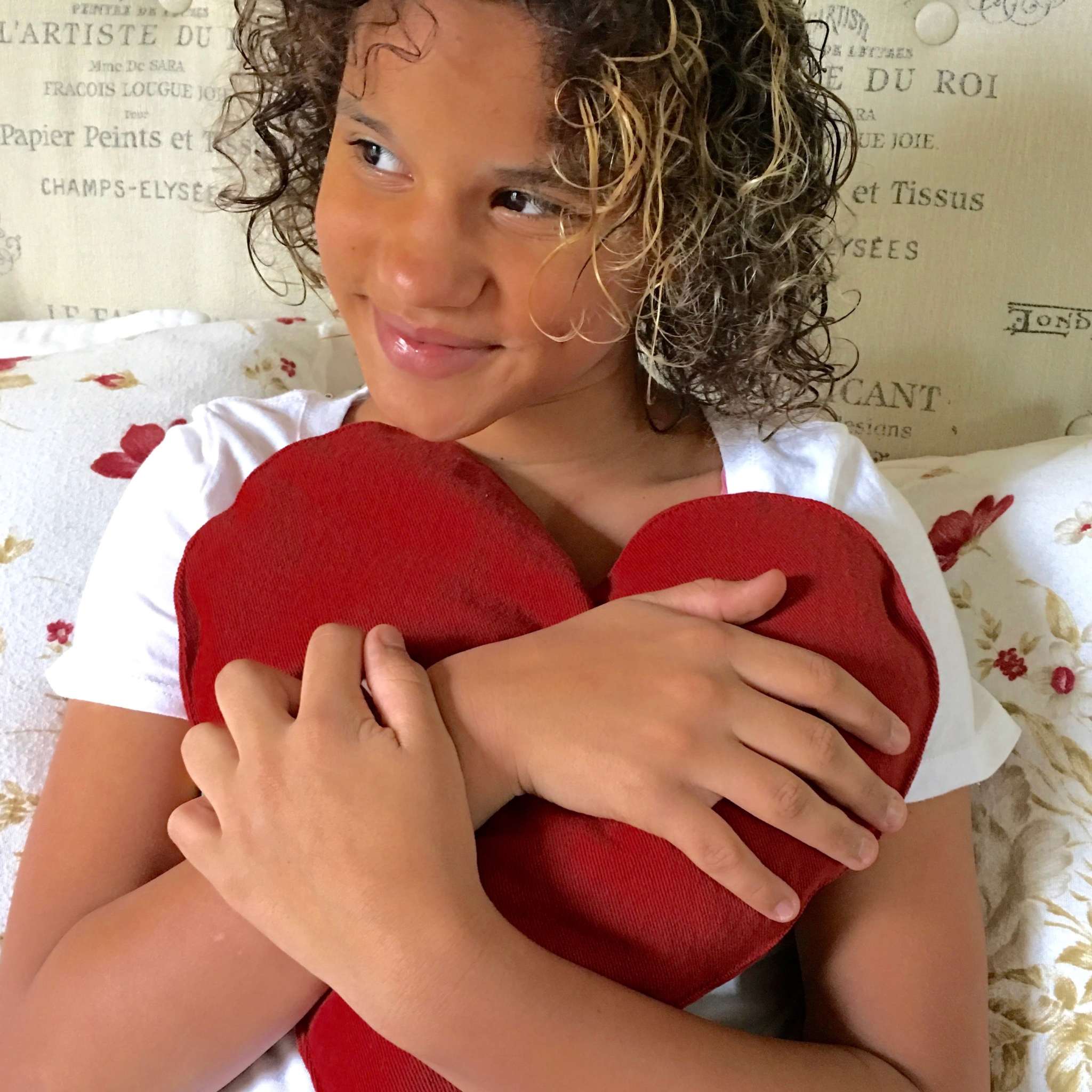 Heart-Shaped Pillow in deep red fabric, with a soft, rounded shape held close in a child's arms