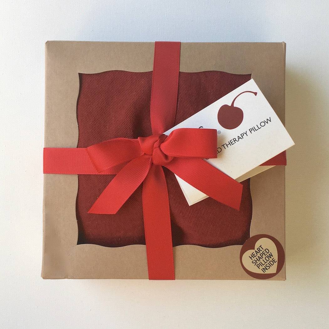 Heart-Shaped Pillow in red textured fabric, packaged in a kraft box tied with a bright red ribbon