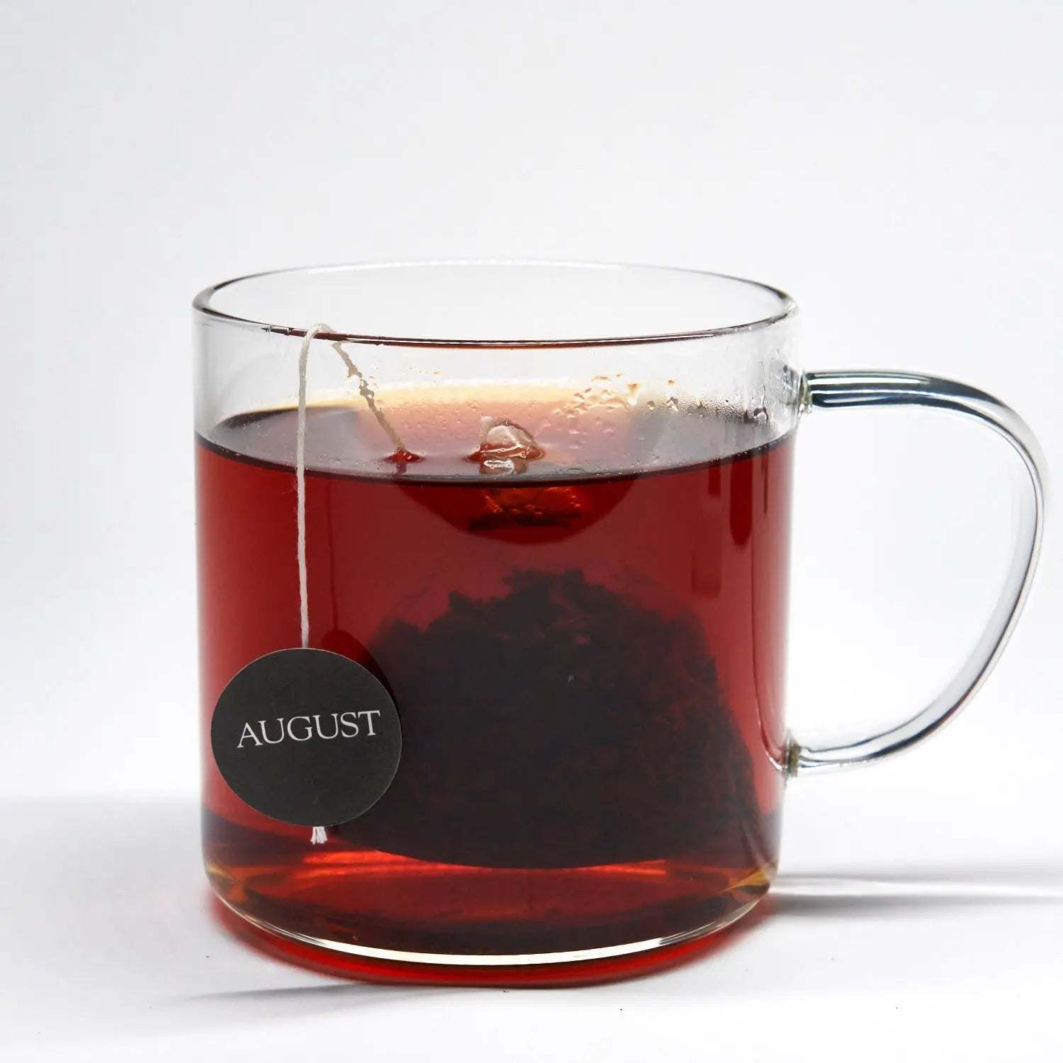 Low Country black tea in a clear glass mug, rich reddish-brown brew with a steeping tea bag and round tag