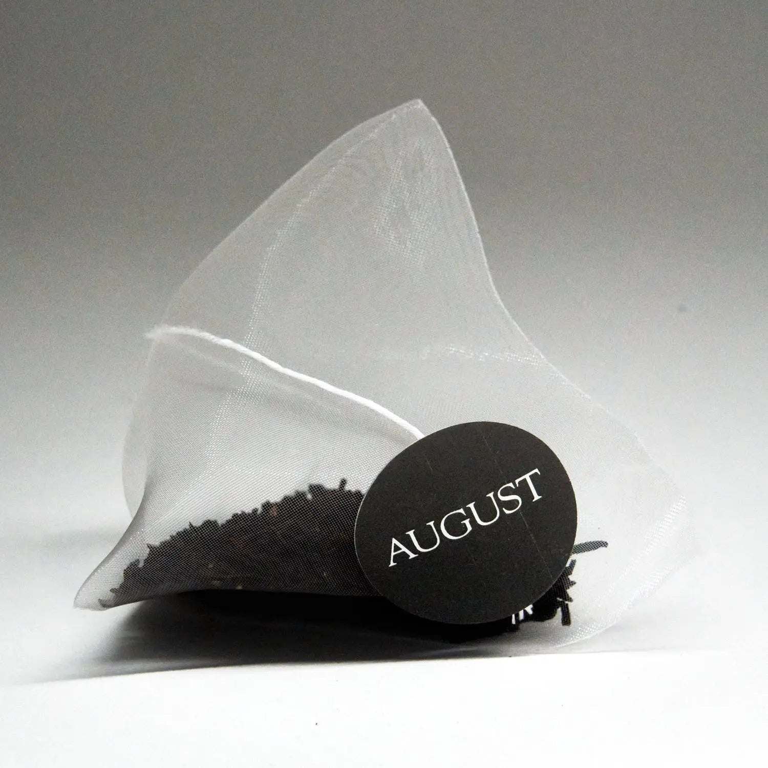 Low Country tea bag made of translucent white mesh, filled with dark loose tea and finished with a black AUGUST tag