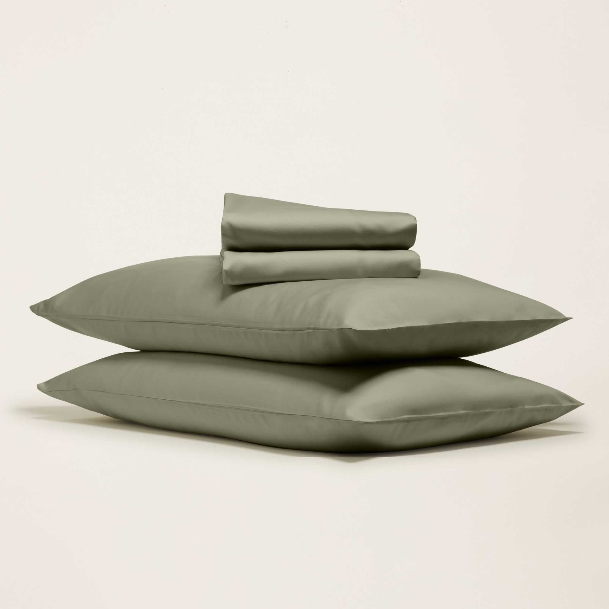 Luxe Australian Sateen Bedding in muted sage green cotton, with two smooth pillowcases stacked beneath folded sheets