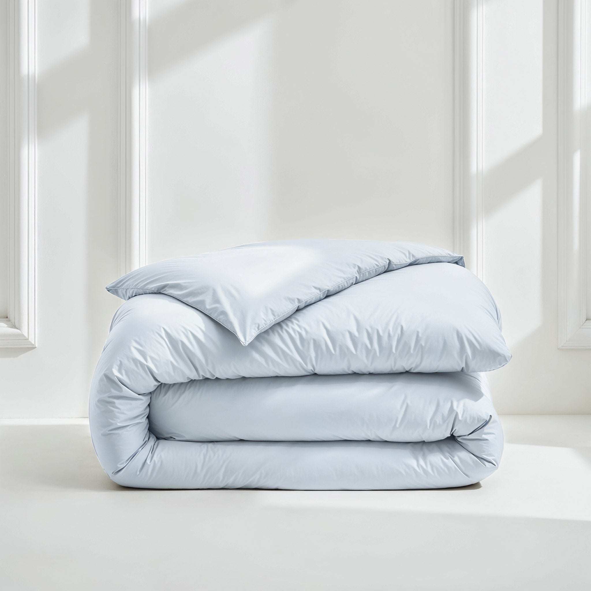 Duvet cover in pale blue sateen cotton with a smooth, subtly lustrous finish, folded into a soft layered stack