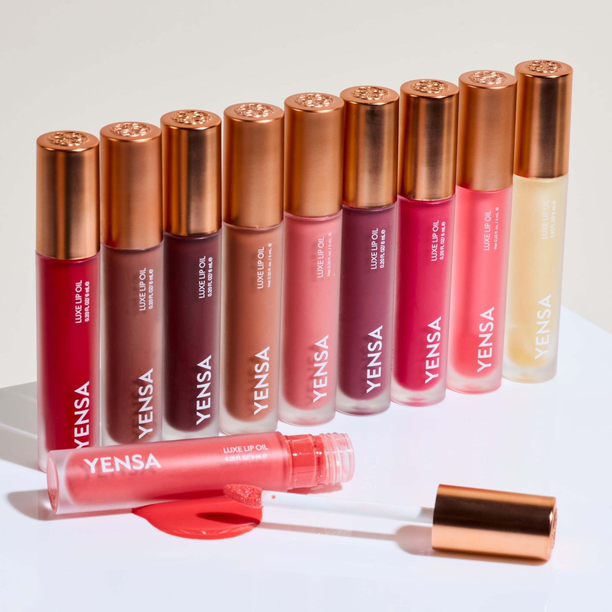 Luxe Lip Nourishing Oil in assorted red, rose, nude and clear shades, displayed in glossy tubes with copper caps