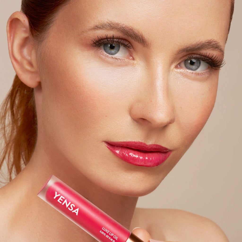 Luxe Lip Nourishing Oil in a coral-pink tube, shown beside glossy bright pink lips with a shiny finish