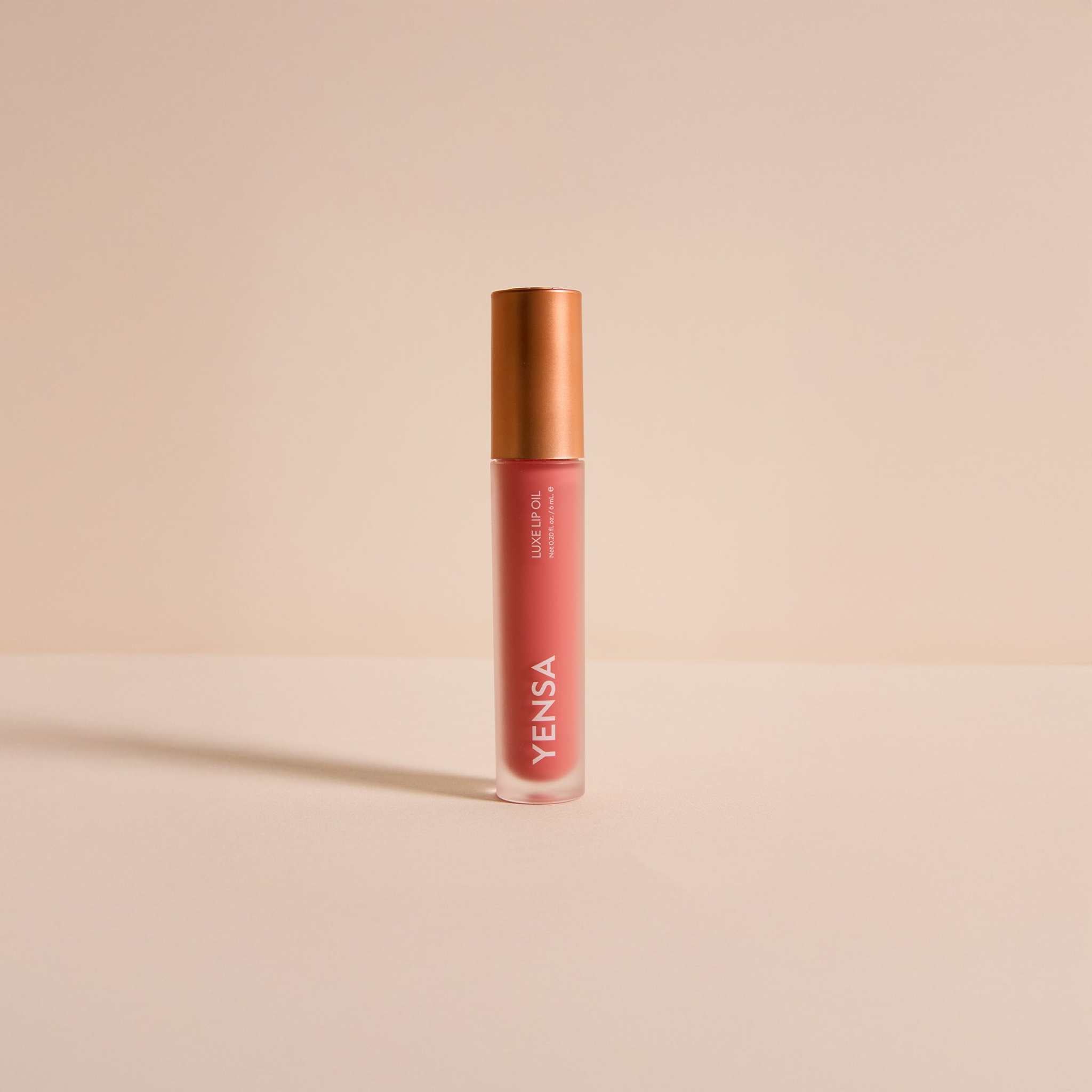 Luxe Lip Nourishing Oil in a coral-pink tube with a copper-toned cap and slim cylindrical design