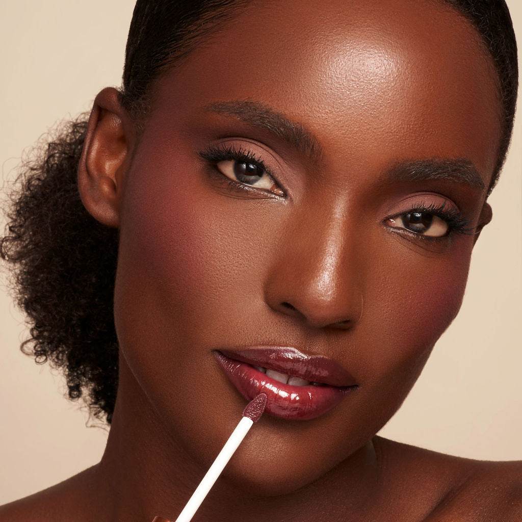 Luxe Lip Nourishing Oil appears as a glossy berry tint applied with a white doe-foot applicator on the lips