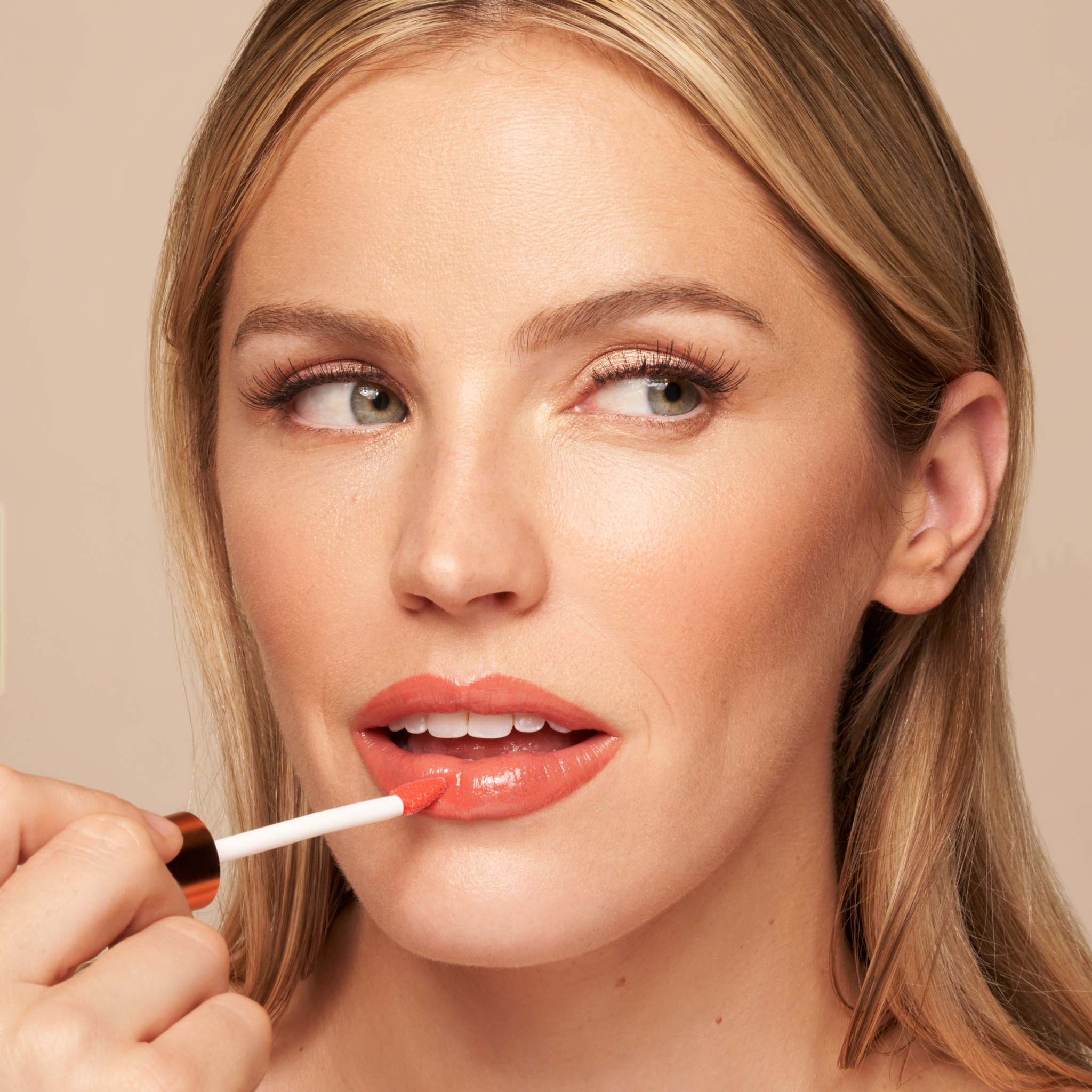 Luxe Lip Nourishing Oil in glossy coral tint, applied with a white wand for a smooth, hydrated finish