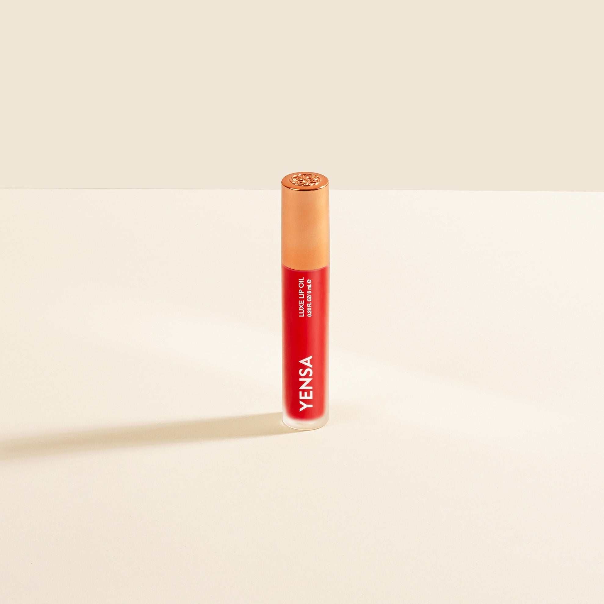 Luxe Lip Nourishing Oil in a slim clear tube with vivid red-orange tinted gloss, white branding and a gold cap.