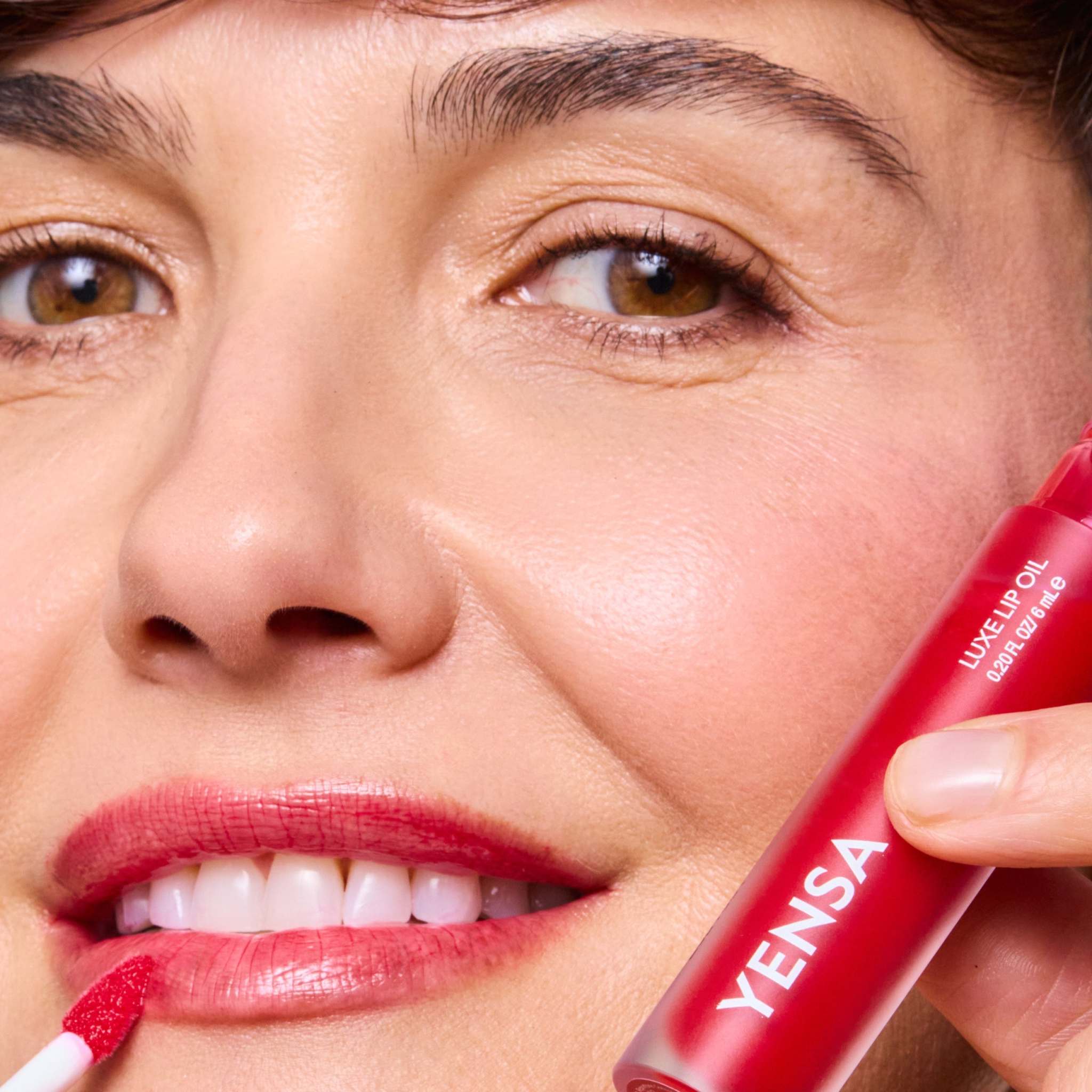 Luxe Lip Nourishing Oil in a bright red tube with a doe-foot applicator applying glossy red tint to lips