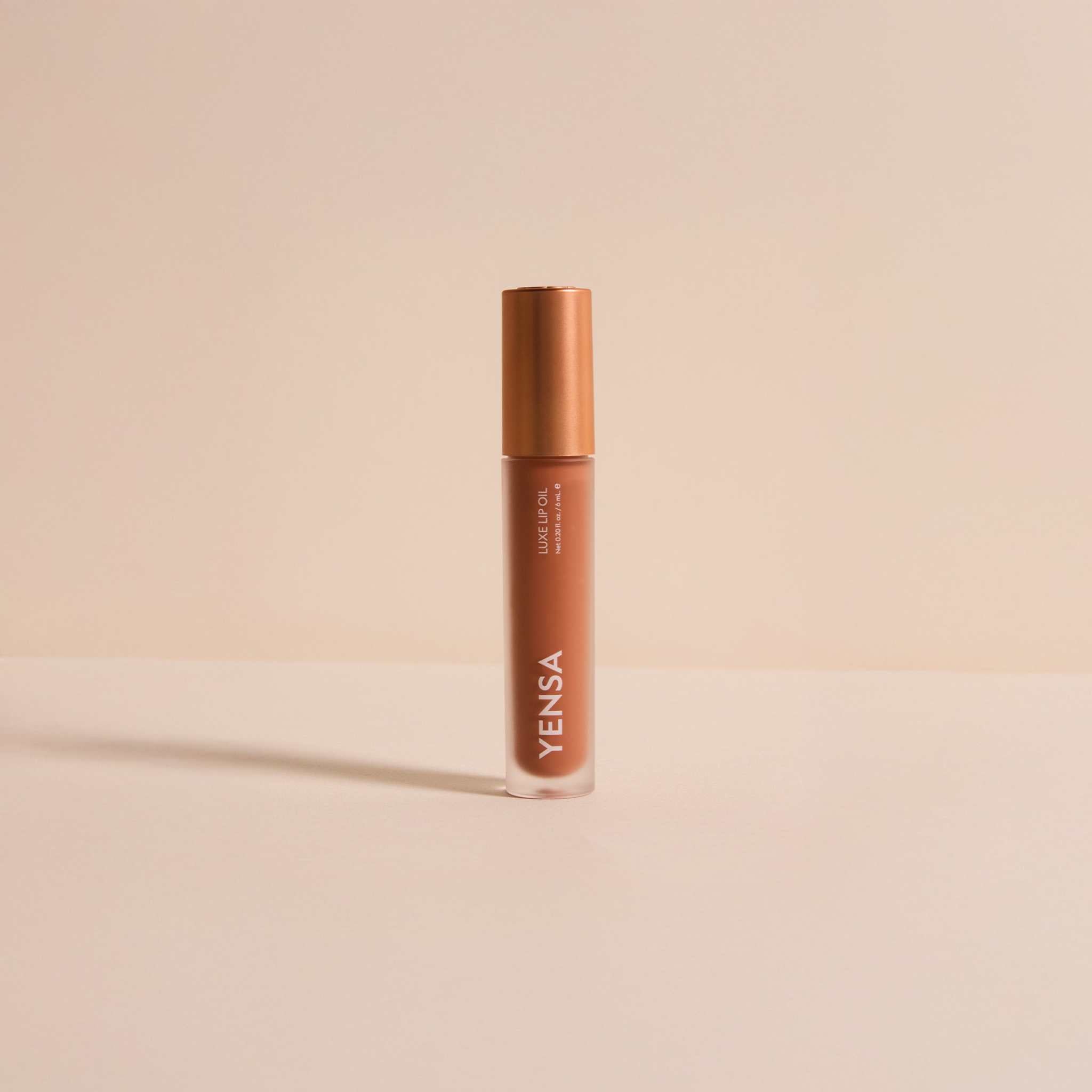 Luxe Lip Nourishing Oil in a clear tube of warm rosy-brown gloss with a metallic copper cap and white lettering