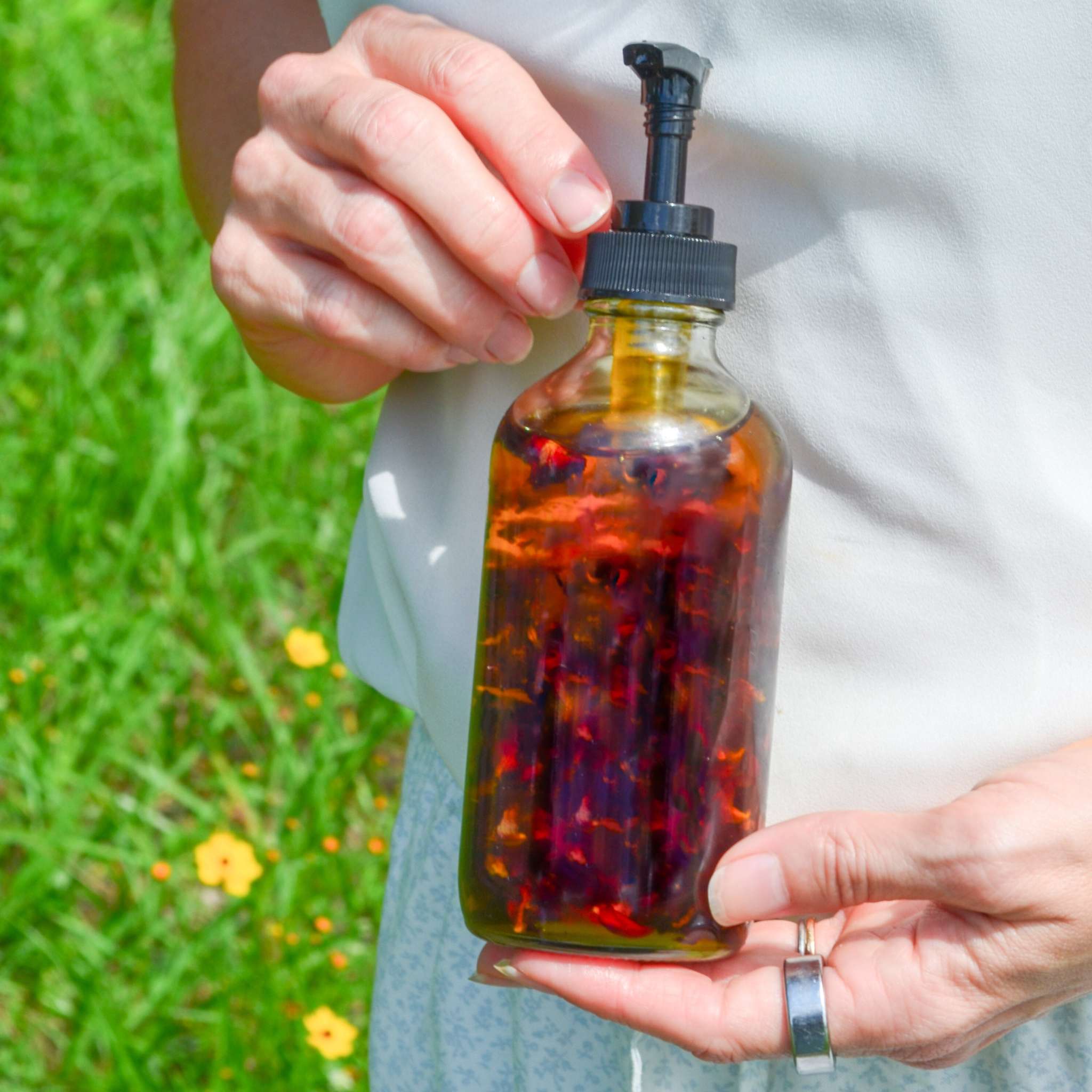 Lymph Love Body Massage Oil in a clear glass pump bottle with amber botanical-infused oil and flower petals