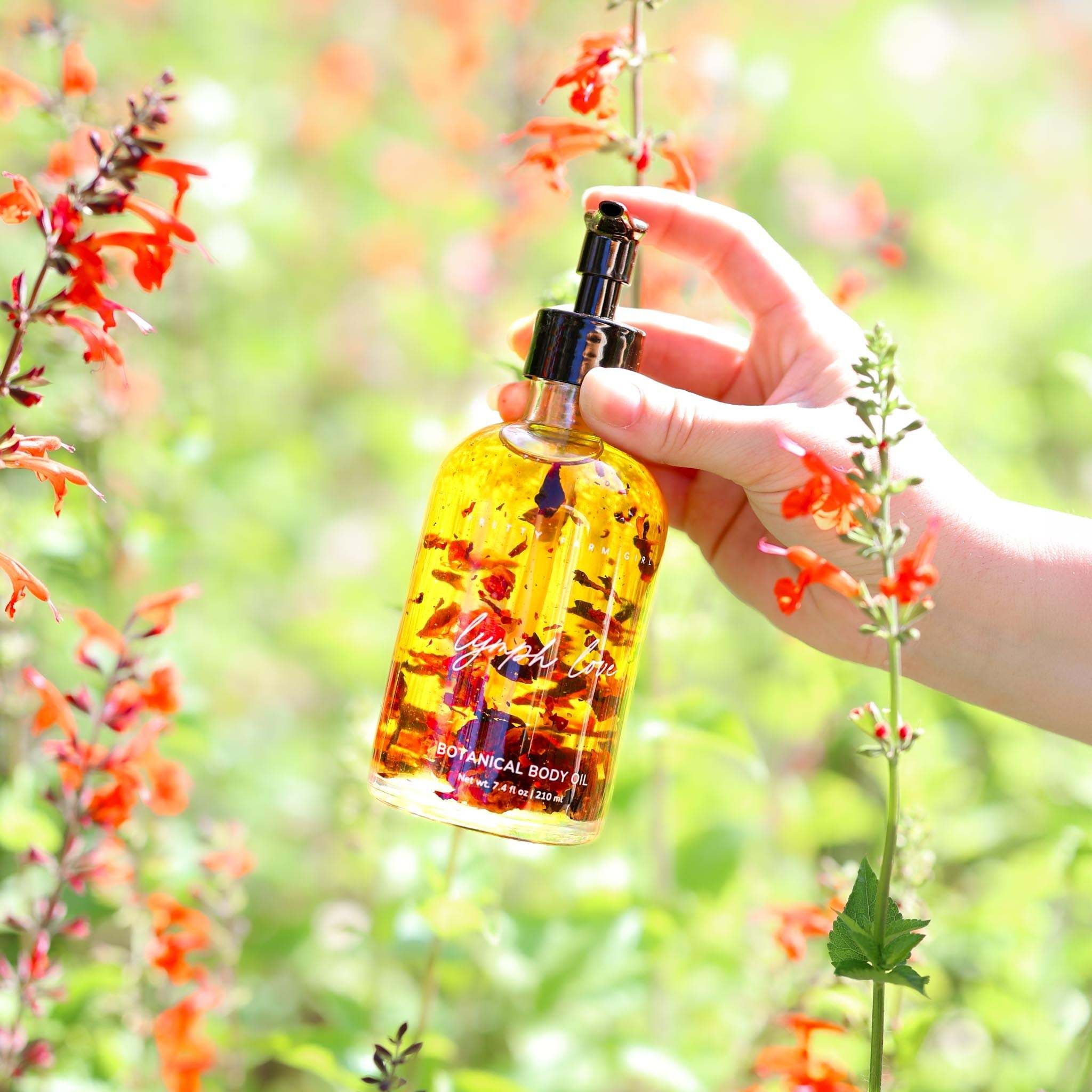 Lymph Love Body Massage Oil in a clear glass pump bottle, golden botanical-infused oil with visible flower petals