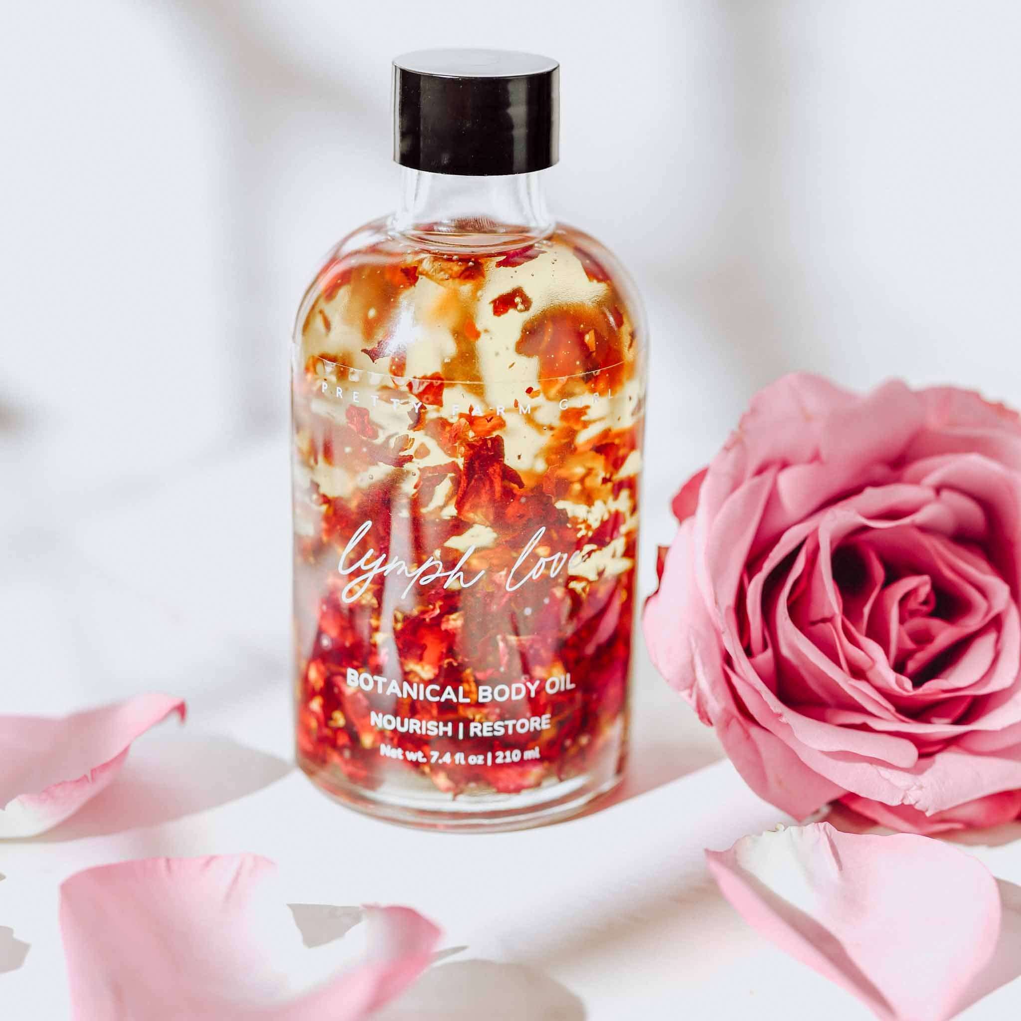 Lymph Love Body Massage Oil in a clear glass bottle with black cap, amber oil and visible red rose botanicals