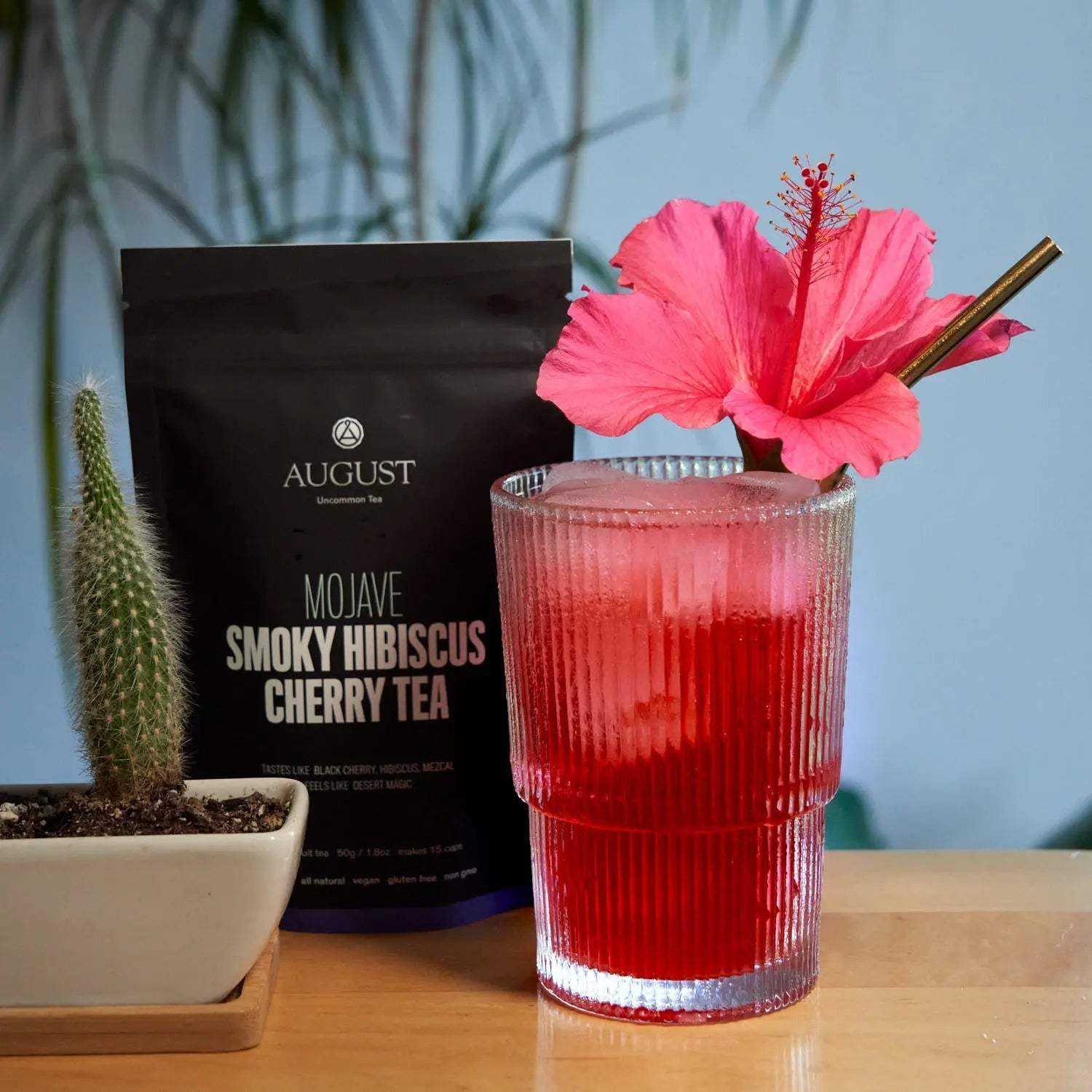 Mojave - Smoky Hibiscus Cherry Tea in a black package beside a vivid red iced drink garnished with hibiscus