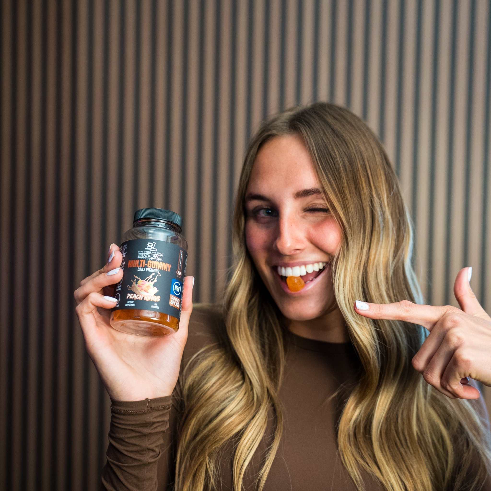 MULTI GUMMY vitamin supplement in a dark bottle, shown with a woman holding an orange gummy