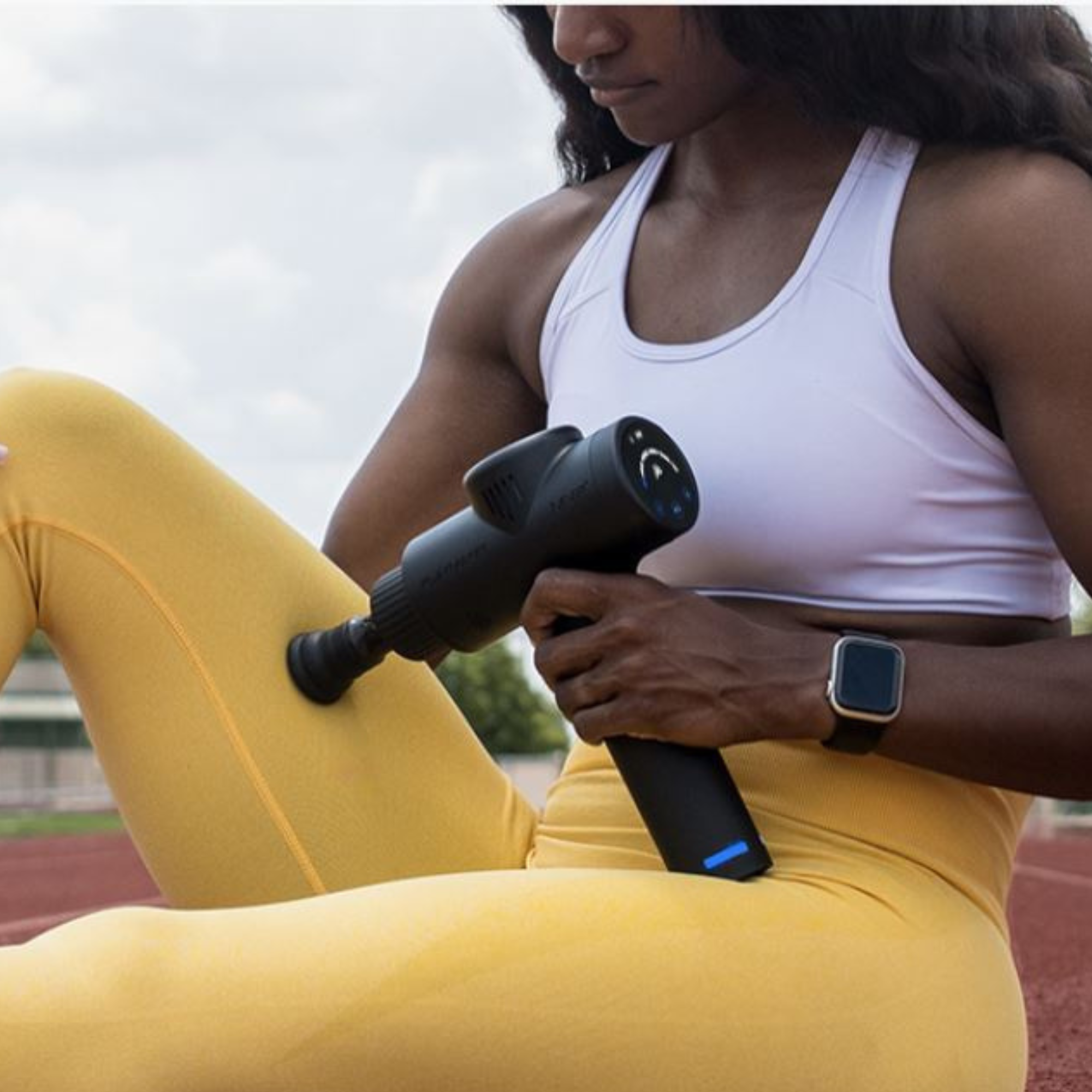 MVP+ Percussion Massage System black handheld massager with round attachment used on yellow leggings