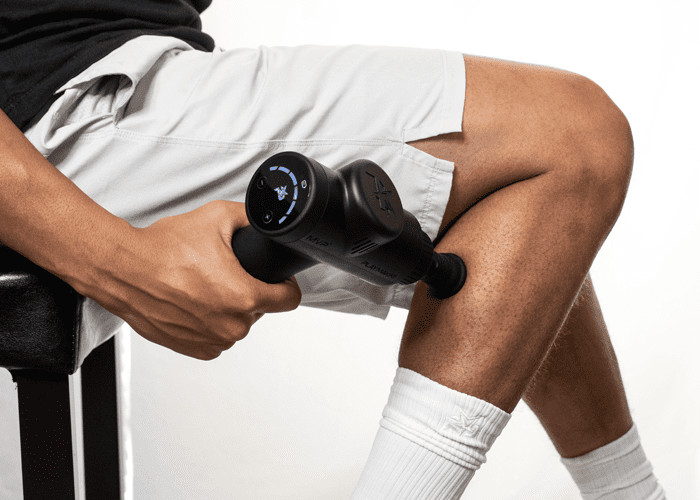 MVP+ Percussion Massage System, black handheld deep-tissue massager with dual rounded heads in use on a thigh