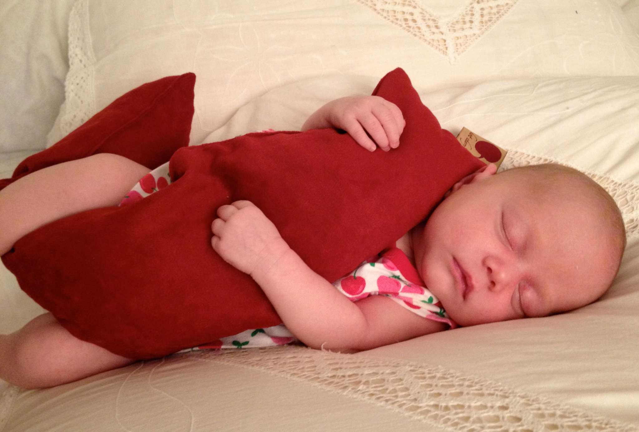 Neck Wrap in rich red plush fabric, a soft elongated cushion cradled by a sleeping baby
