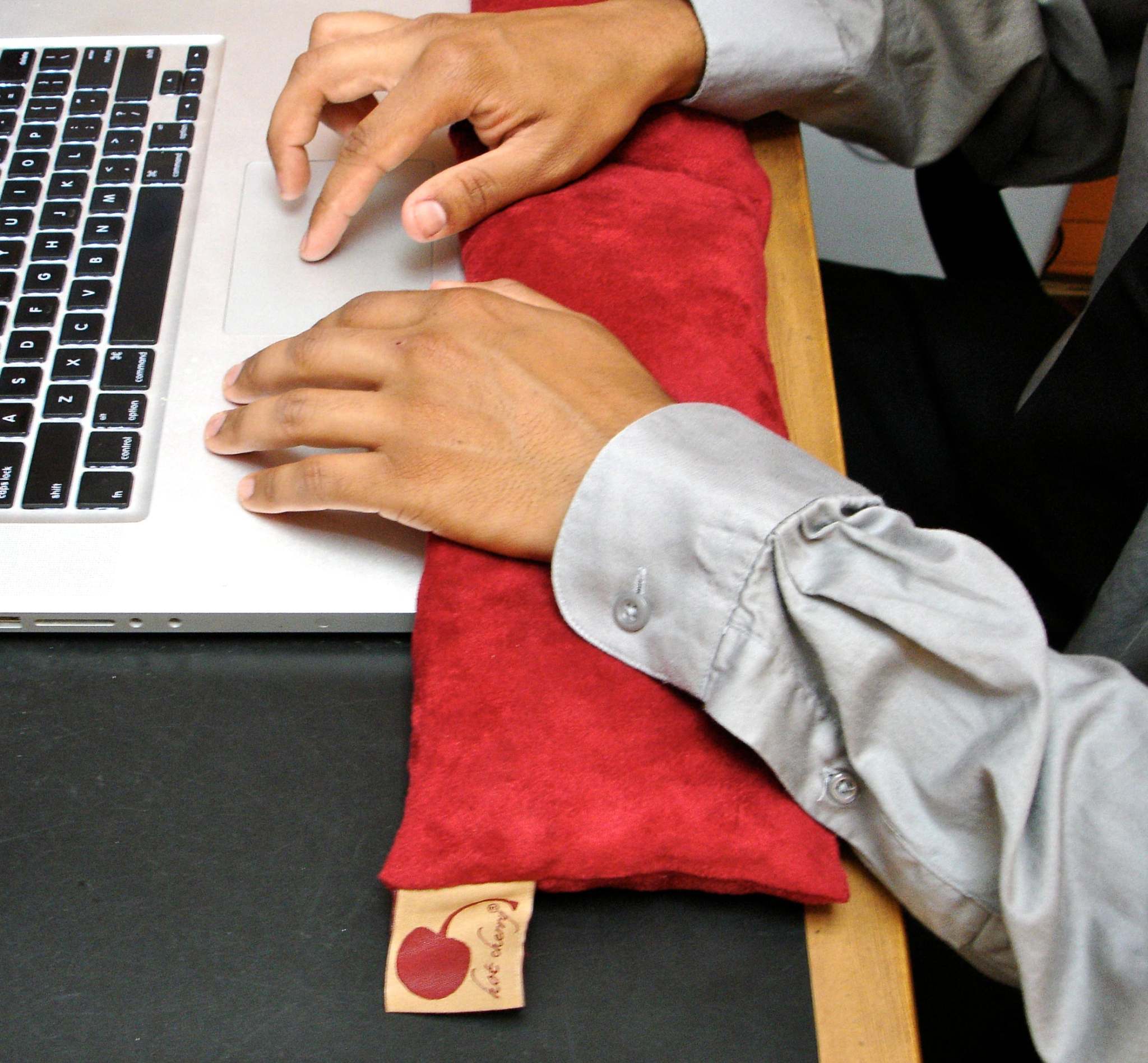 Neck Wrap in plush red ultra-suede, a long rectangular pillow with a soft textured surface and fabric tag