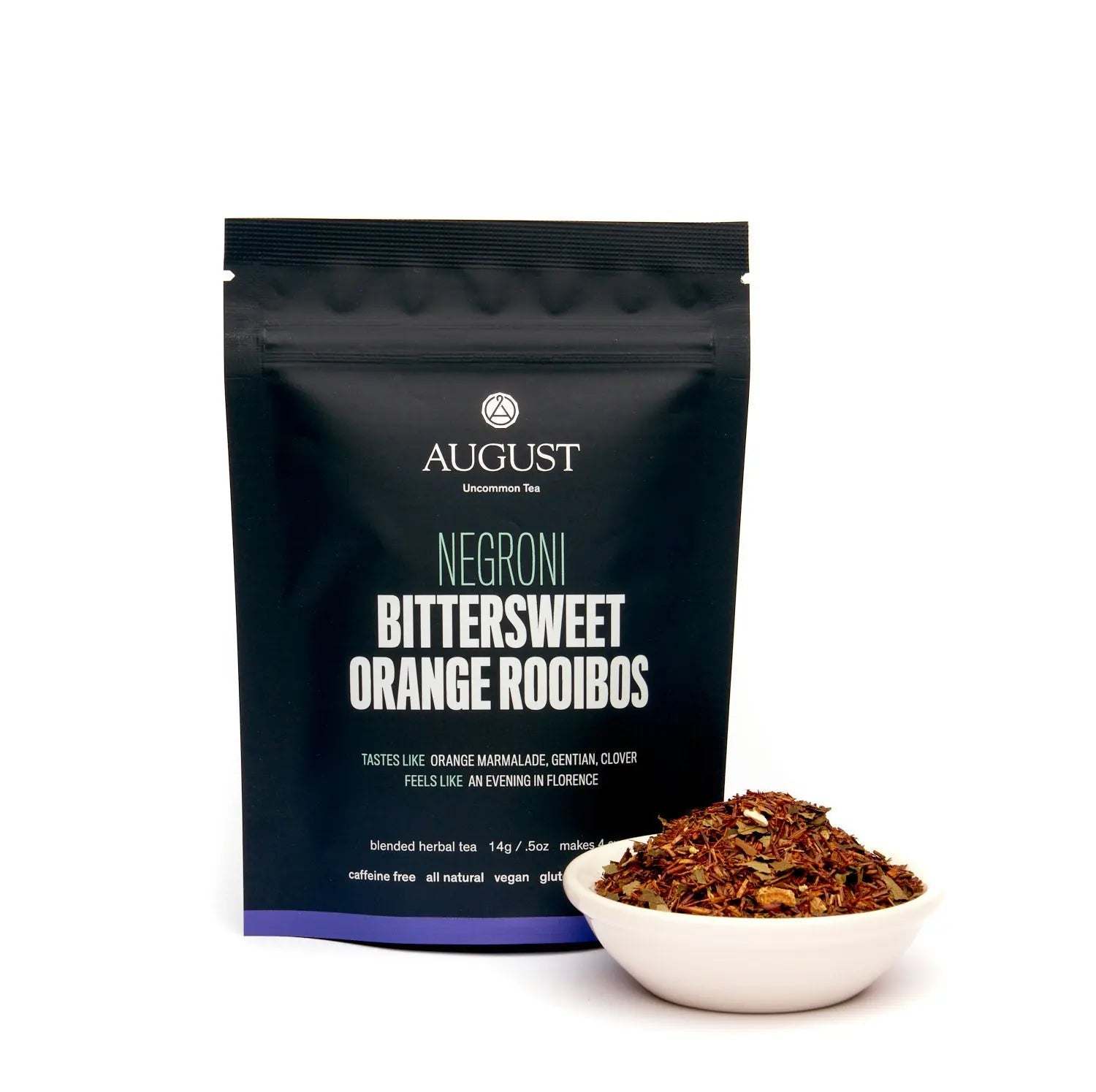 Negroni rooibos tea in a matte black pouch beside loose reddish-brown tea leaves in a white bowl