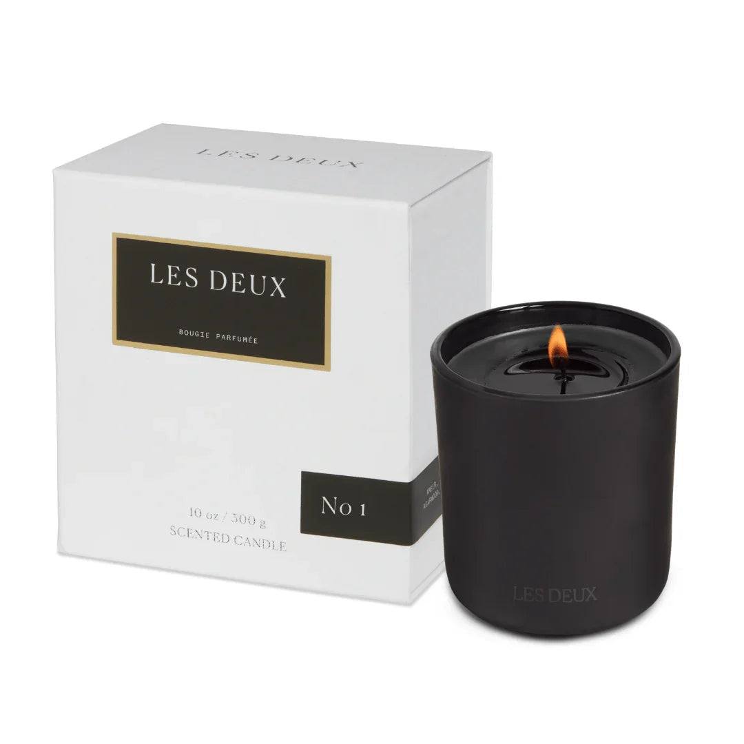 No. 1 - Bois Sacré Candle in a matte black vessel with a lit wick, alongside its white branded box