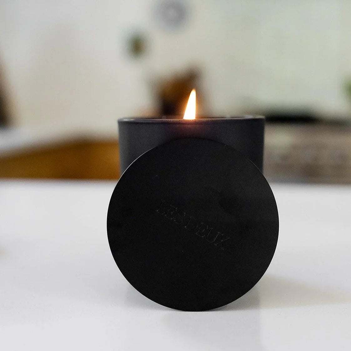 No. 1 - Bois Sacré Candle in a matte black container with a lit flame and matching round lid displayed in front