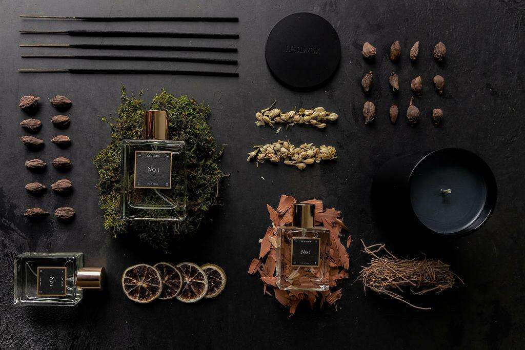 No. 1 - Bois Sacré Perfume in clear glass bottles with black labels, surrounded by moss, spices, wood chips, and dried botanicals