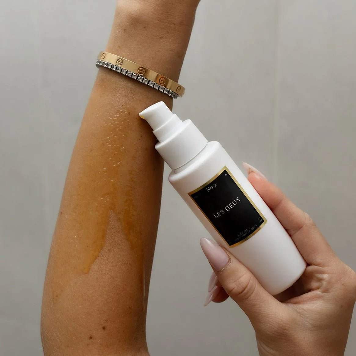 No. 2 - Peau d’Or Body Oil in a white pump bottle, shown with golden oil on skin and a black label