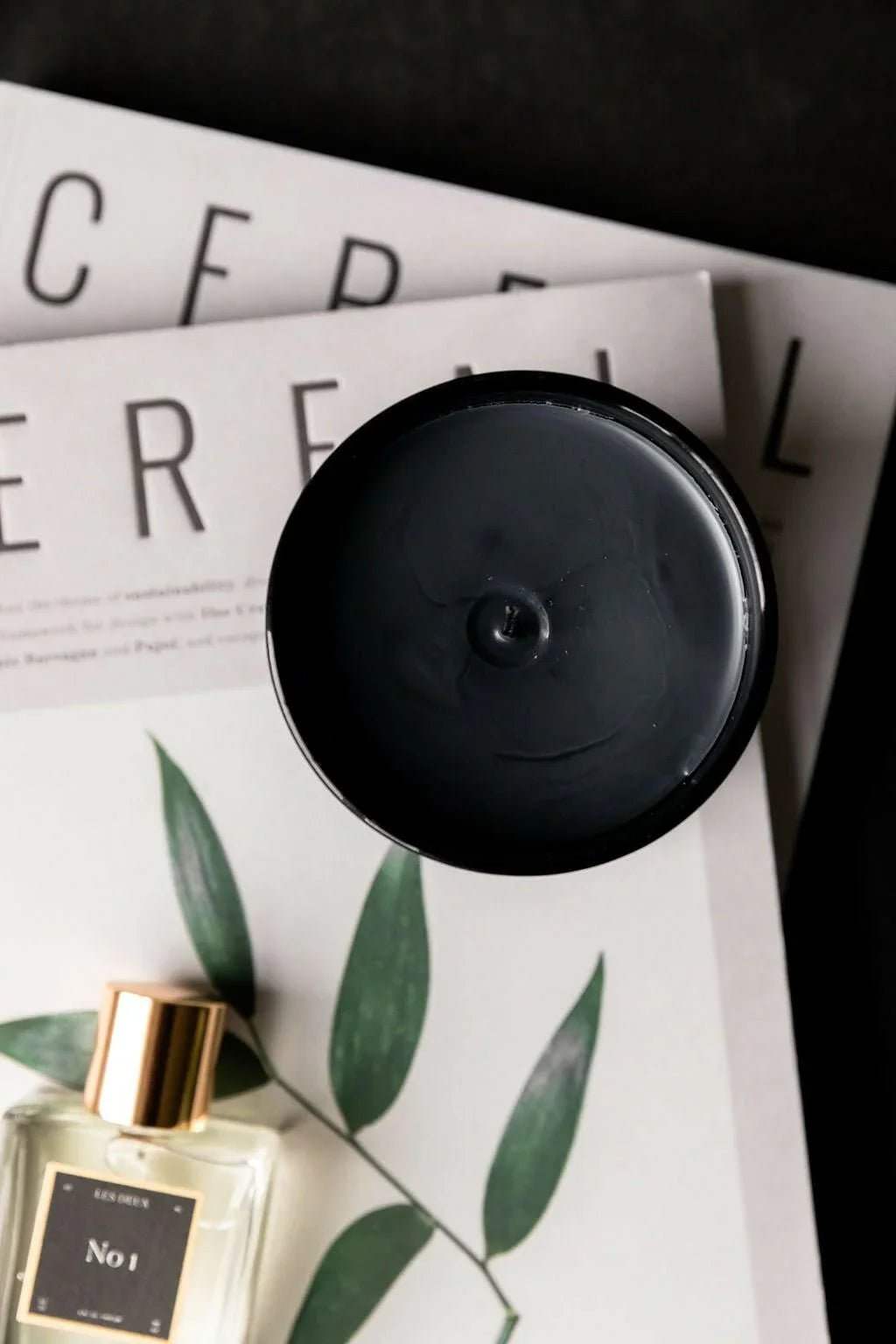 No. 3 - Brume Ardente Candle, black round lid shown above a botanical magazine and No. 1 fragrance bottle