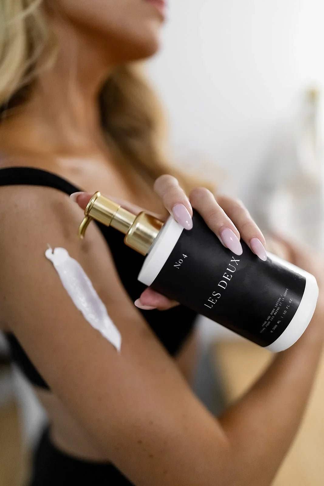 No. 4 - L'Âme Velours Body Lotion in a black bottle with gold pump and white label, shown being applied to skin