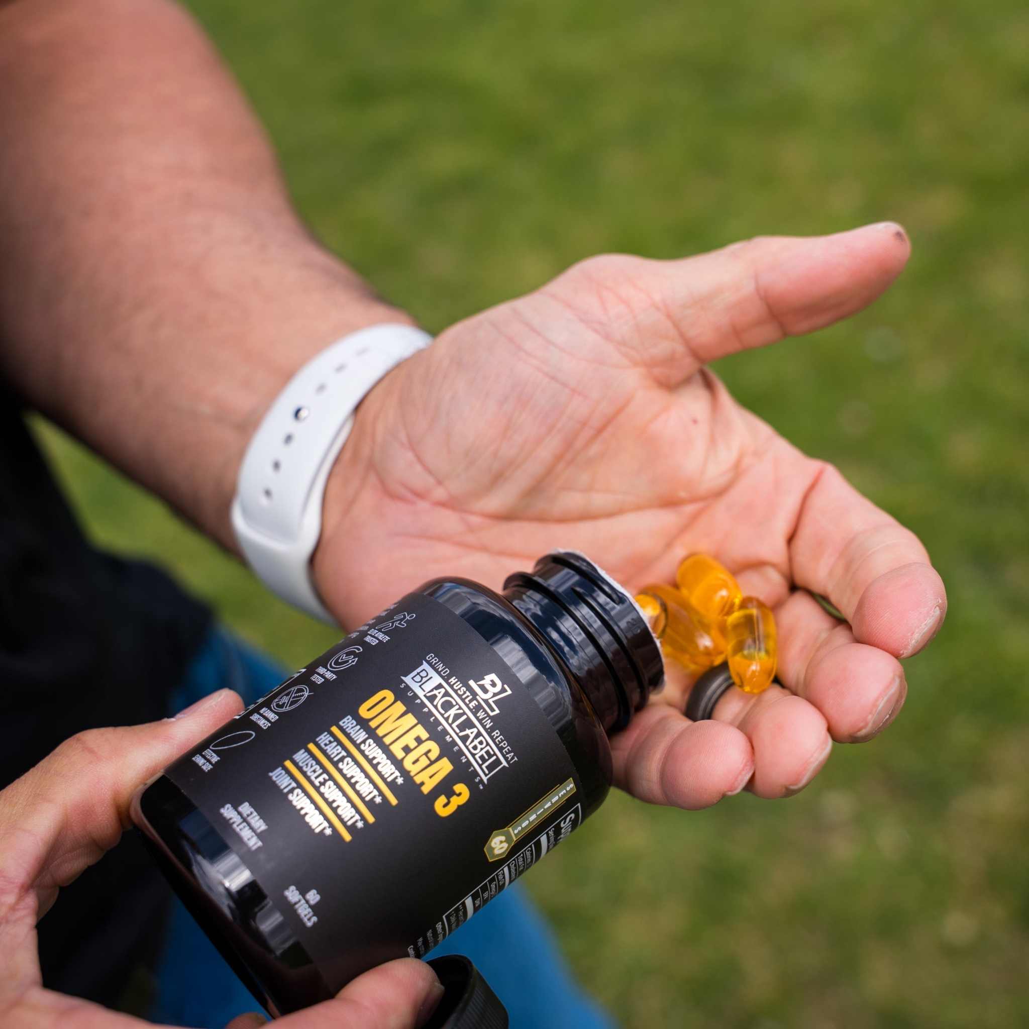 Omega-3 Fatty Acids supplement with a black bottle and amber softgel capsules spilling into an open hand