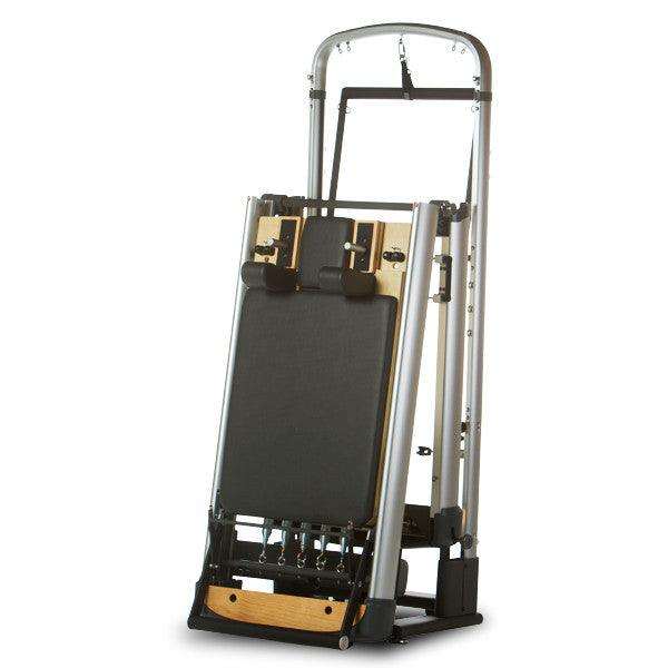 Peak PilateSystem® Deluxe Bundle folding reformer in black and silver with wooden accents, compact and upright for easy storage.