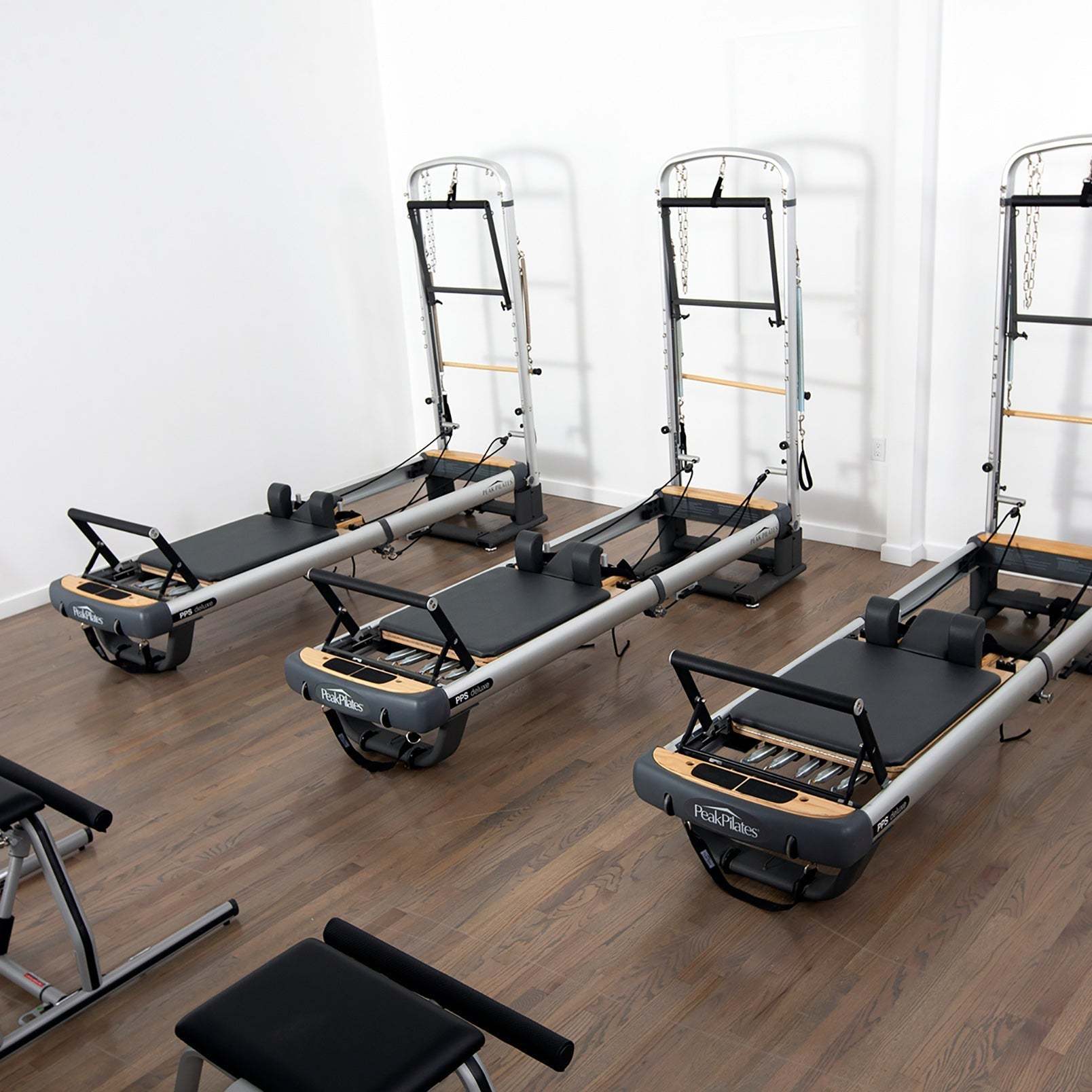 Peak PilateSystem® Deluxe Bundle featuring black and grey reformer Pilates machines with folding towers and padded platforms on wood flooring.